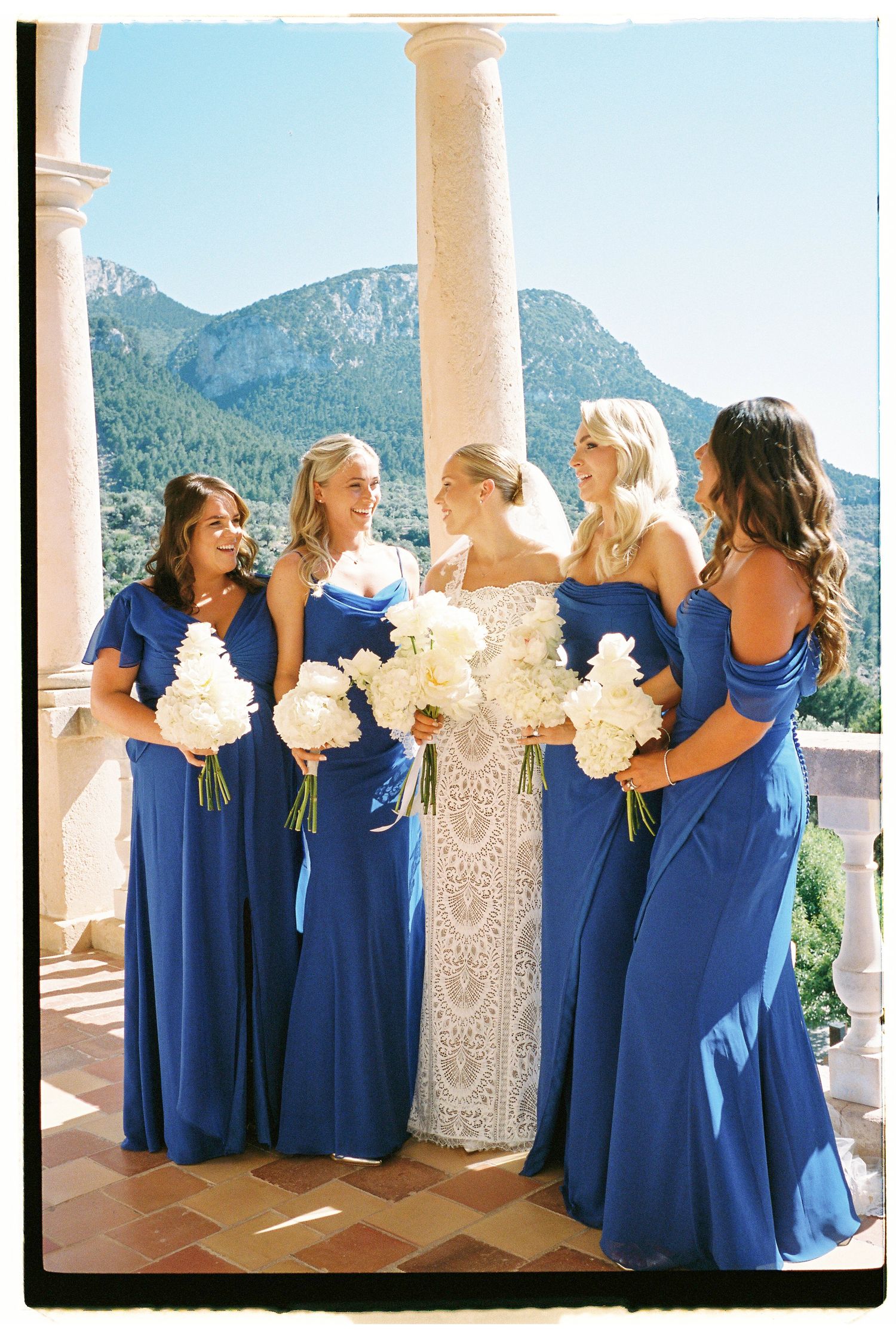 Wedding party in royal blue dresses and white gowns pose against mountain backdrop.