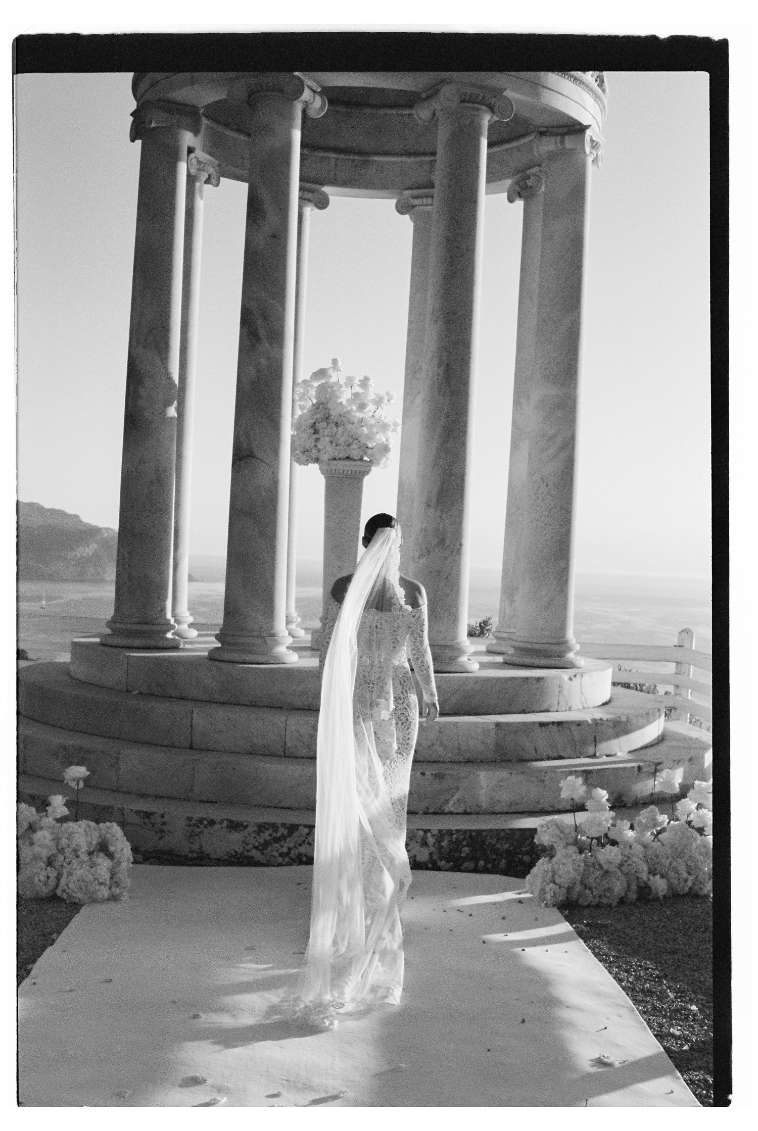 Ethereal black and white photo of bride among classical columns with flowing veil.