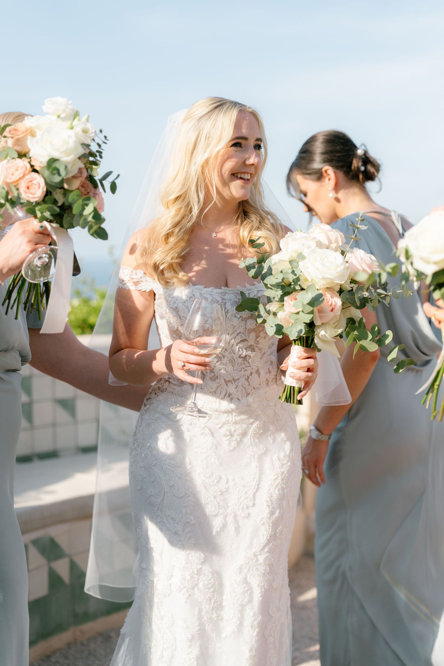 Wedding party in light gray and white attire celebrating outdoors on a sunny day.