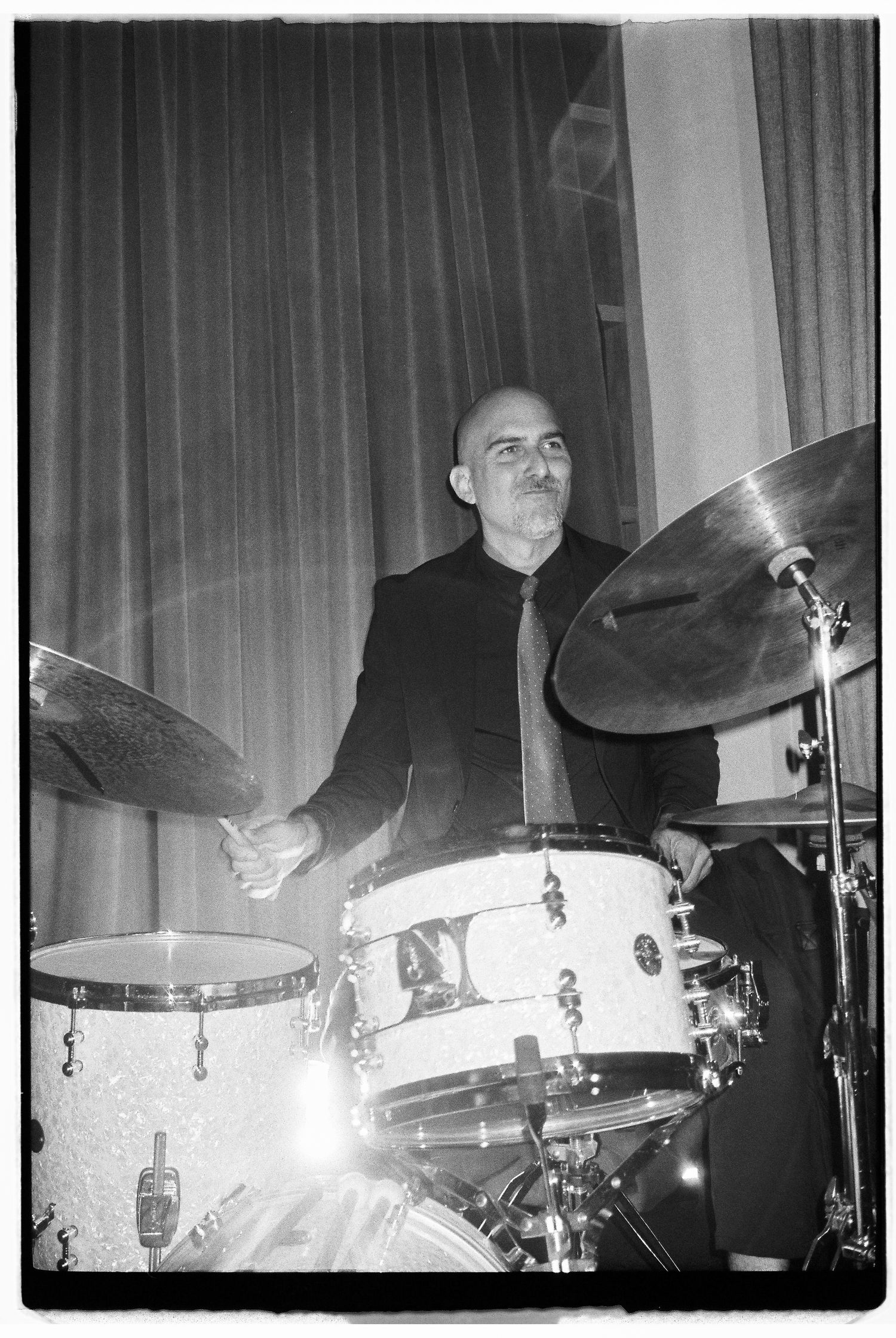 Drummer performing on a white drum kit in black and white photography.
