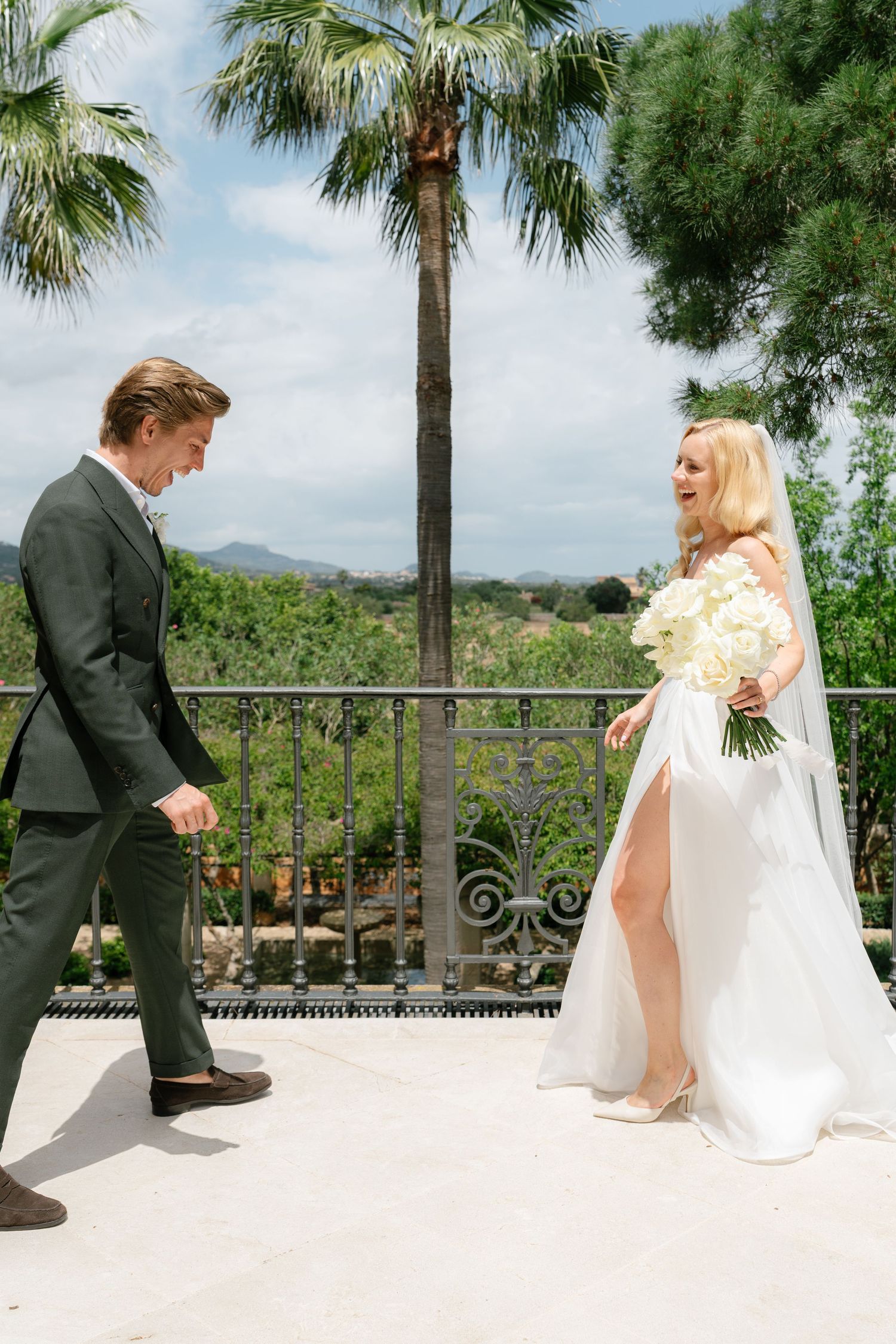 Wedding first look sequence on a sunny terrace with palm trees and mountain backdrop.