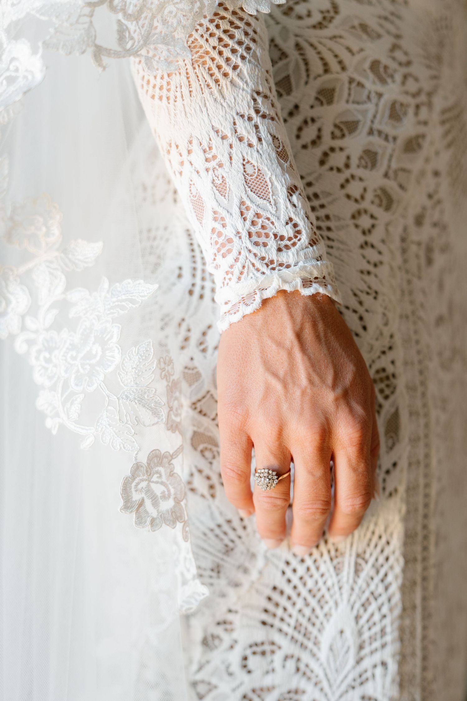 Close-up detail of delicate lace sleeve and wedding ring against white fabric.