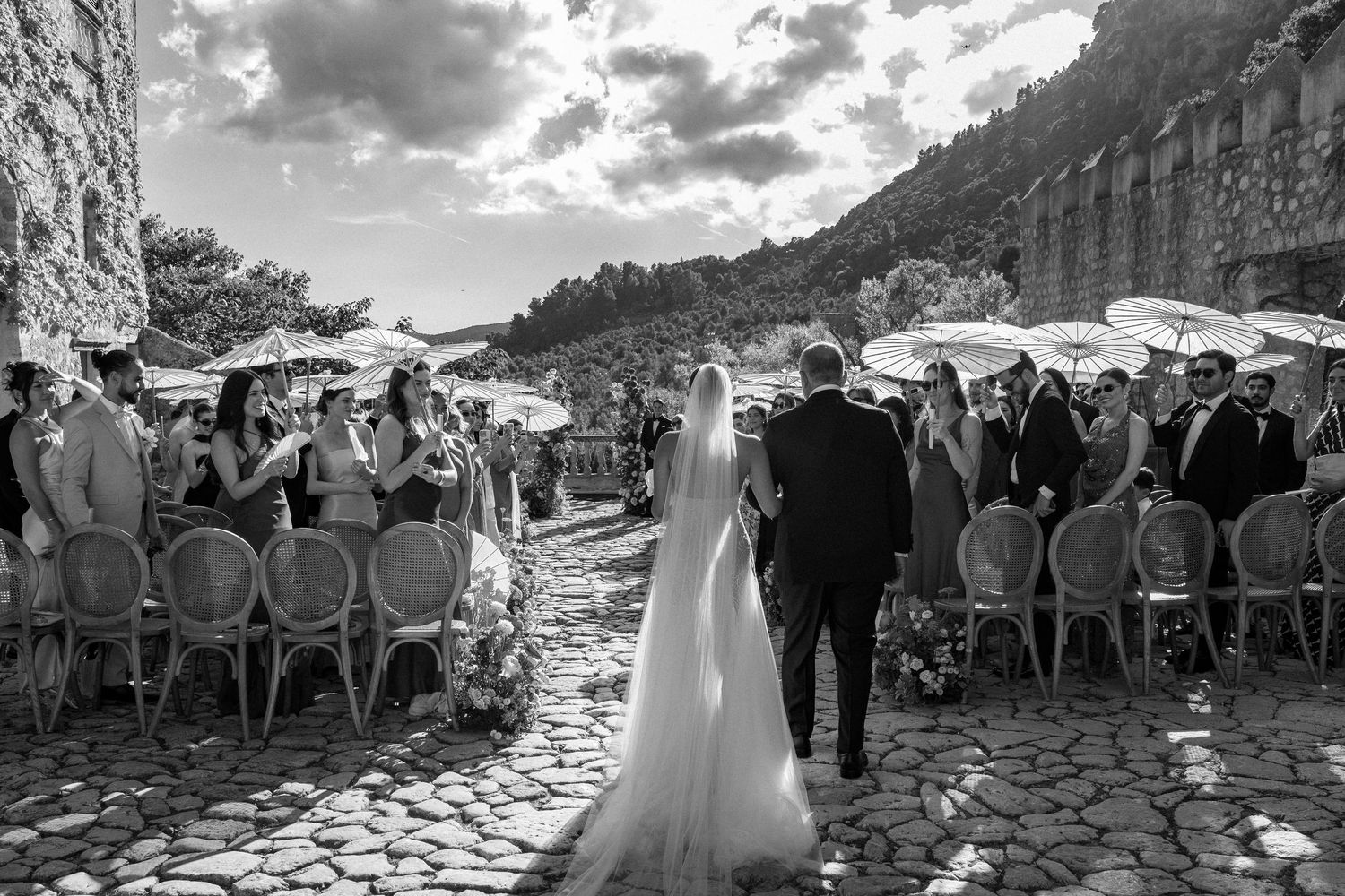 Black and white panoramic view of outdoor wedding ceremony with guests seated under cloudy skies.