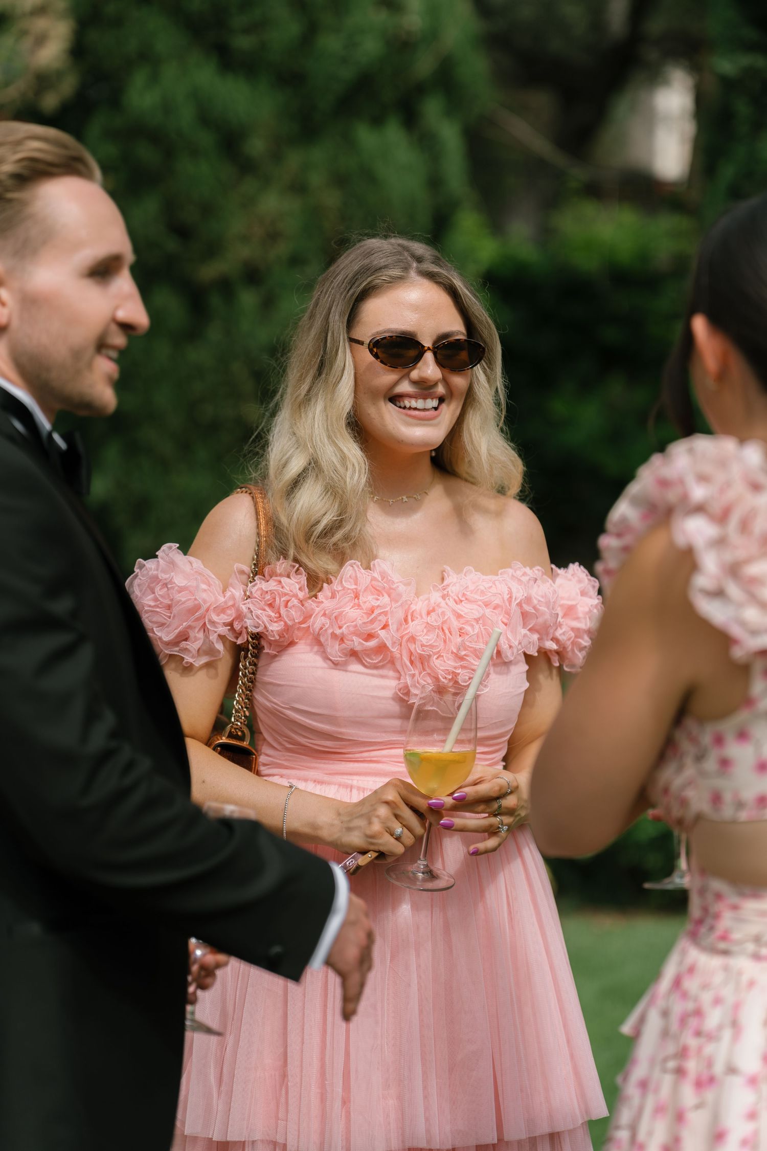 Wedding guests in pink dresses enjoying champagne at an outdoor celebration.
