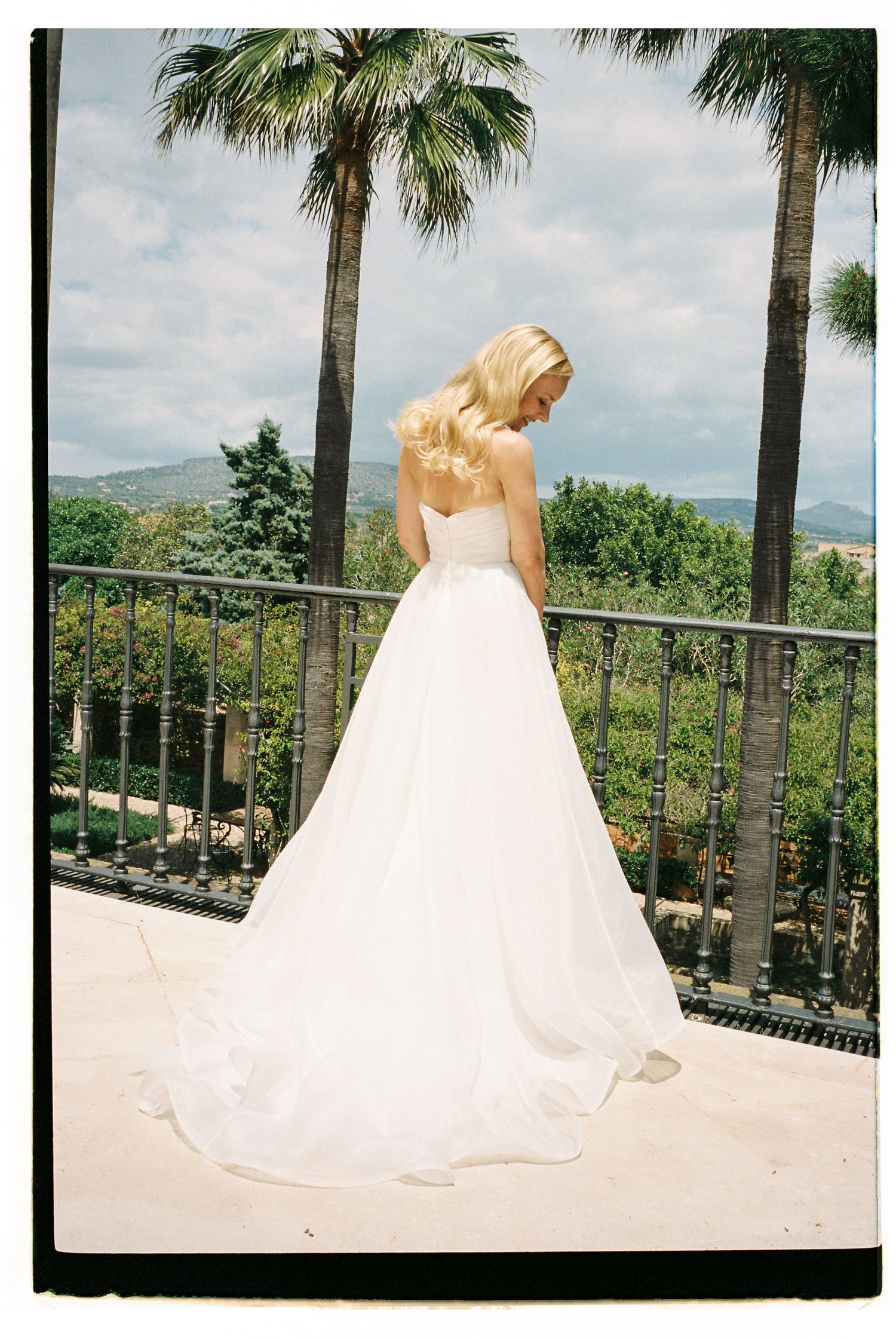 White wedding gown with flowing train photographed against palm trees and mountain backdrop.