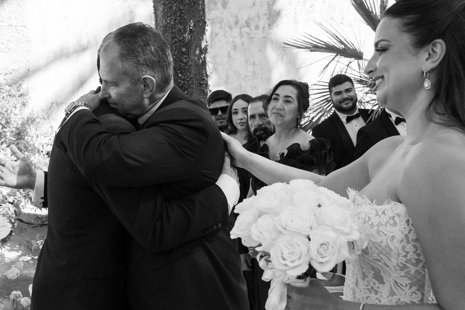 Black and white photo of emotional father hugging bride at wedding ceremony while bridesmaids watch.