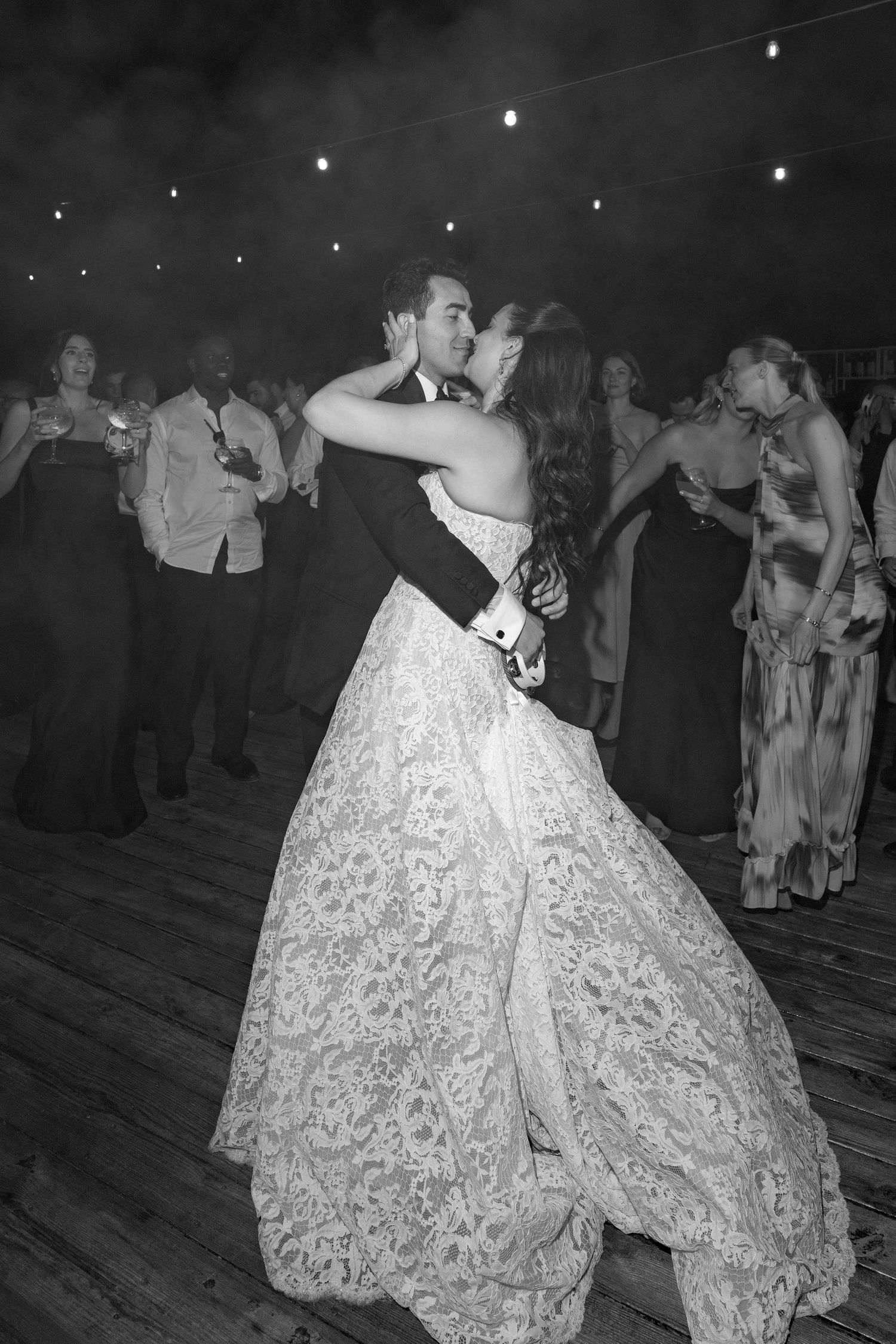 Bride and groom share a first dance kiss in lace wedding gown at romantic black and white reception.