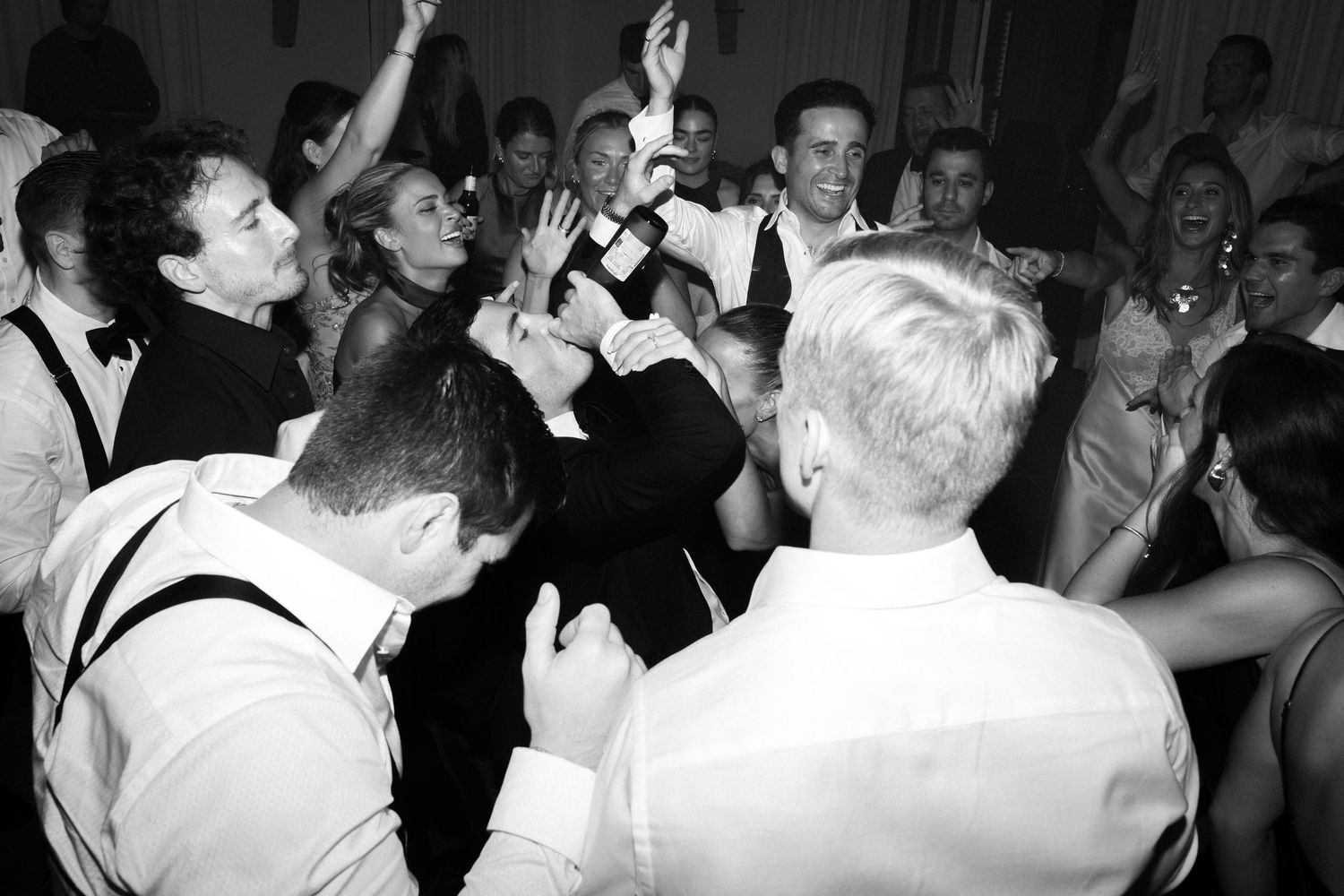 A black and white photo of an energetic crowd celebrating and dancing at what appears to be a party or reception.