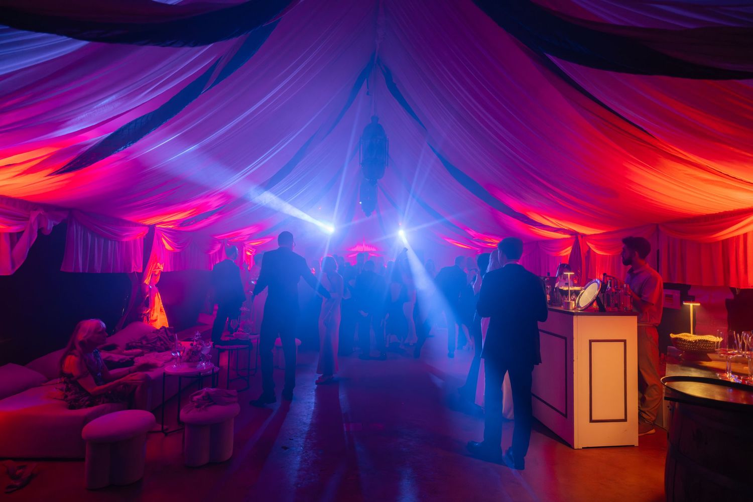 Wedding reception dance floor illuminated with vibrant purple and orange lighting under draped tent ceiling.