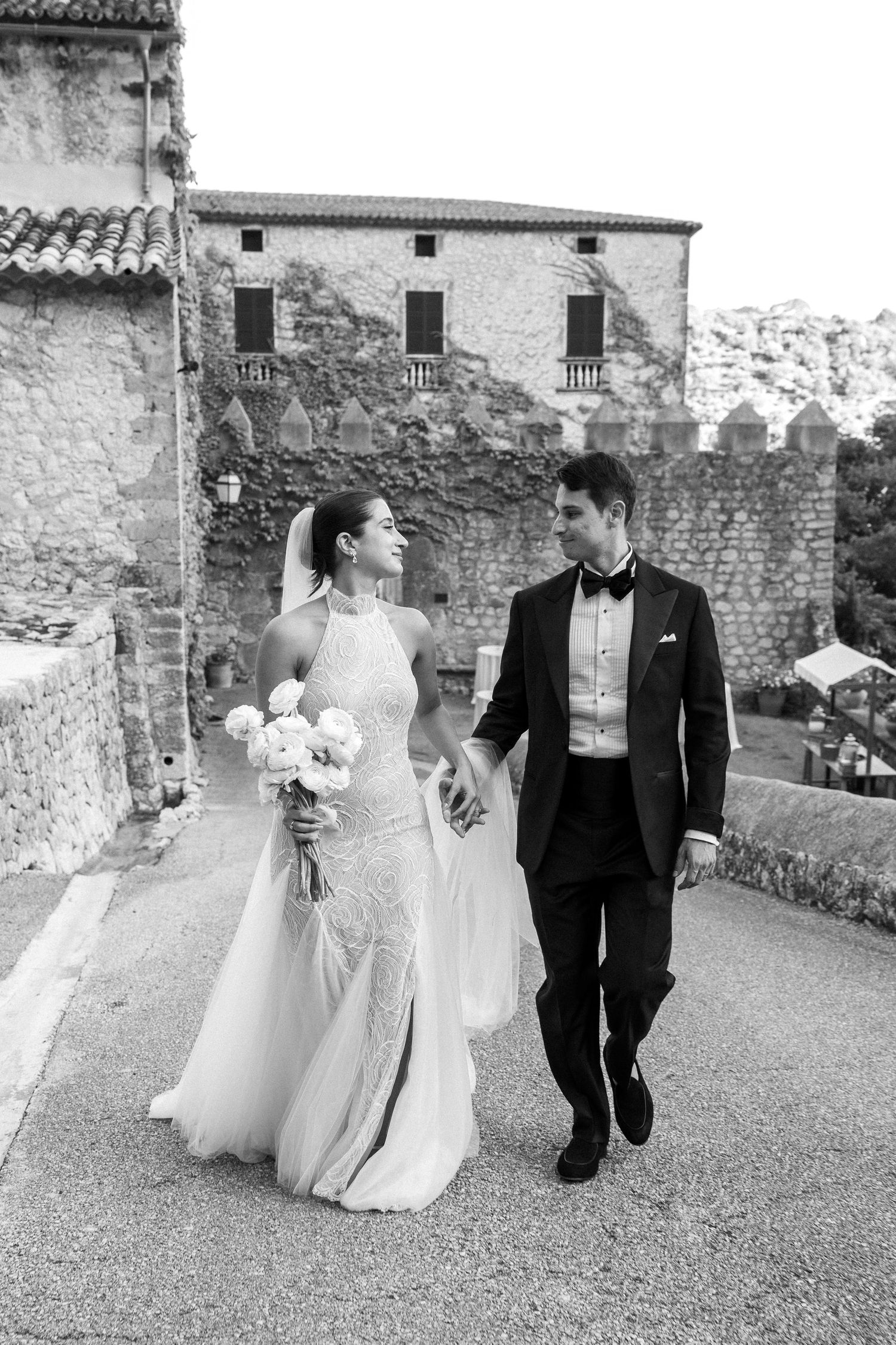 Black and white photo of newlyweds walking together at a historic stone venue.