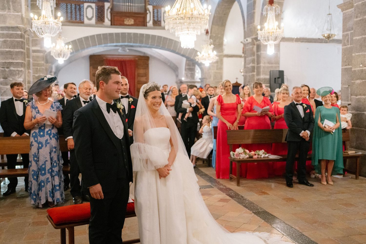 Wedding ceremony in ornate church with crystal chandeliers and traditional decor.