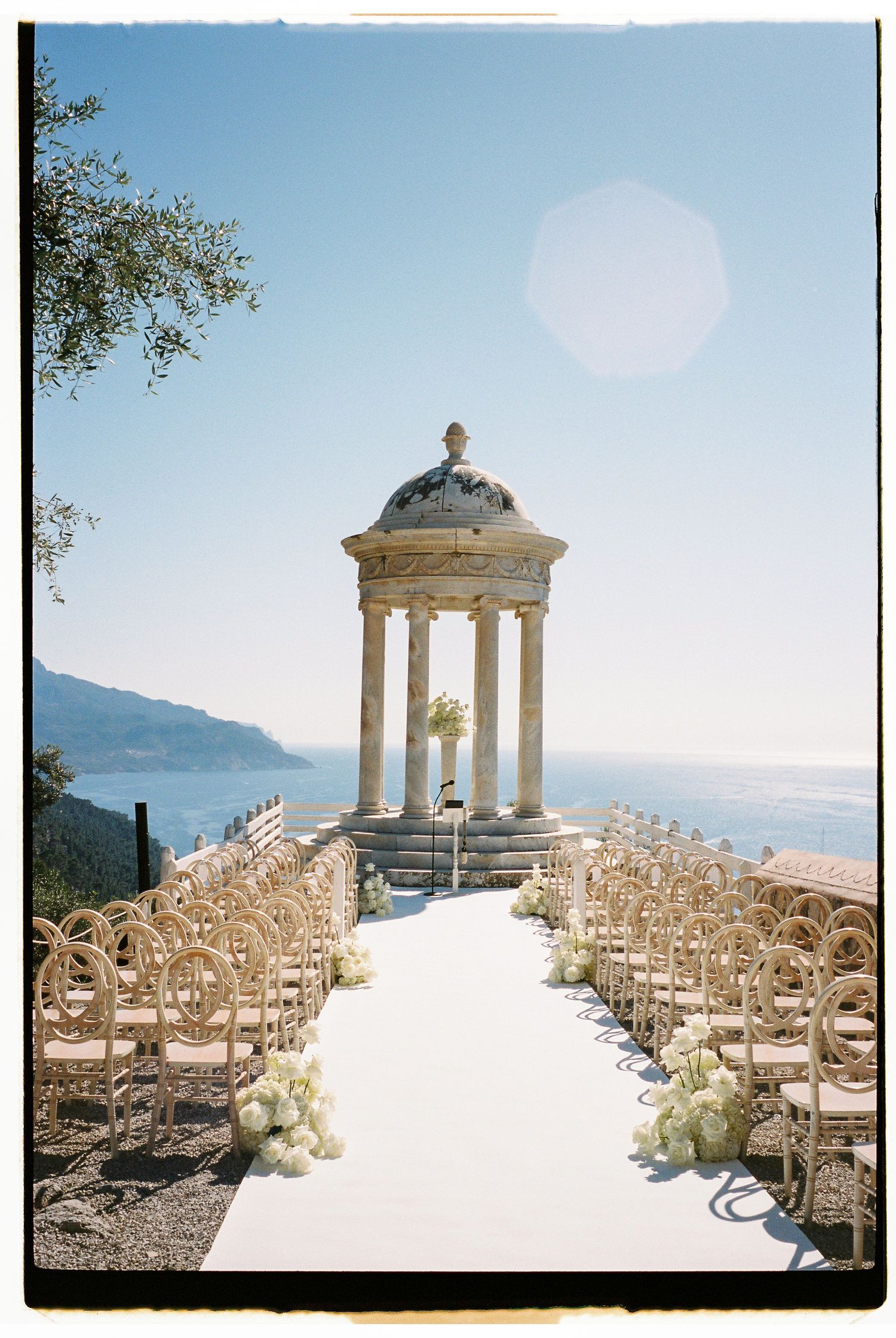 Wedding ceremony setup with white chairs leading to a classical domed gazebo overlooking mountain views.