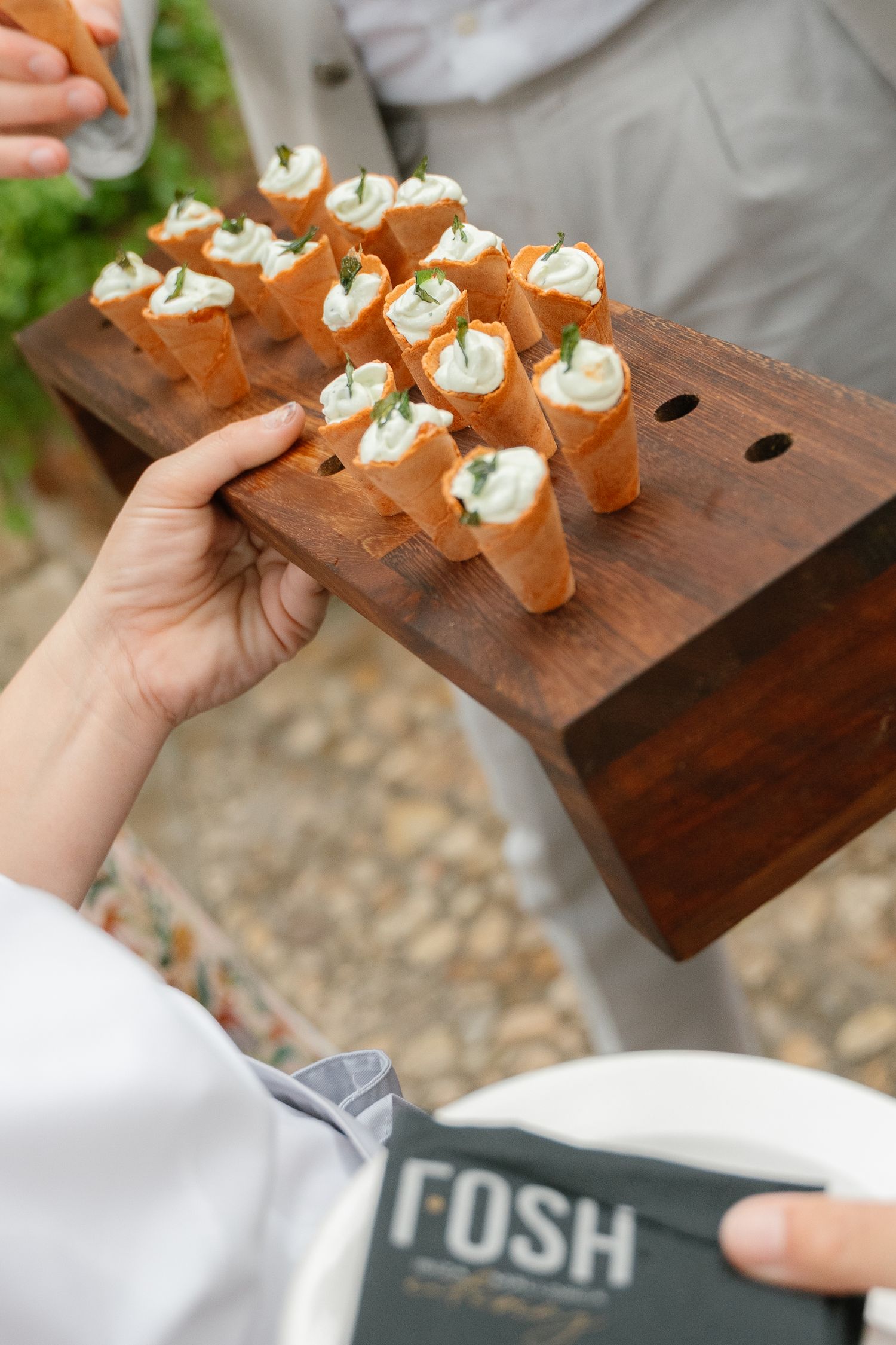 Wooden serving board displays a row of elegant appetizers topped with cream at an outdoor event.