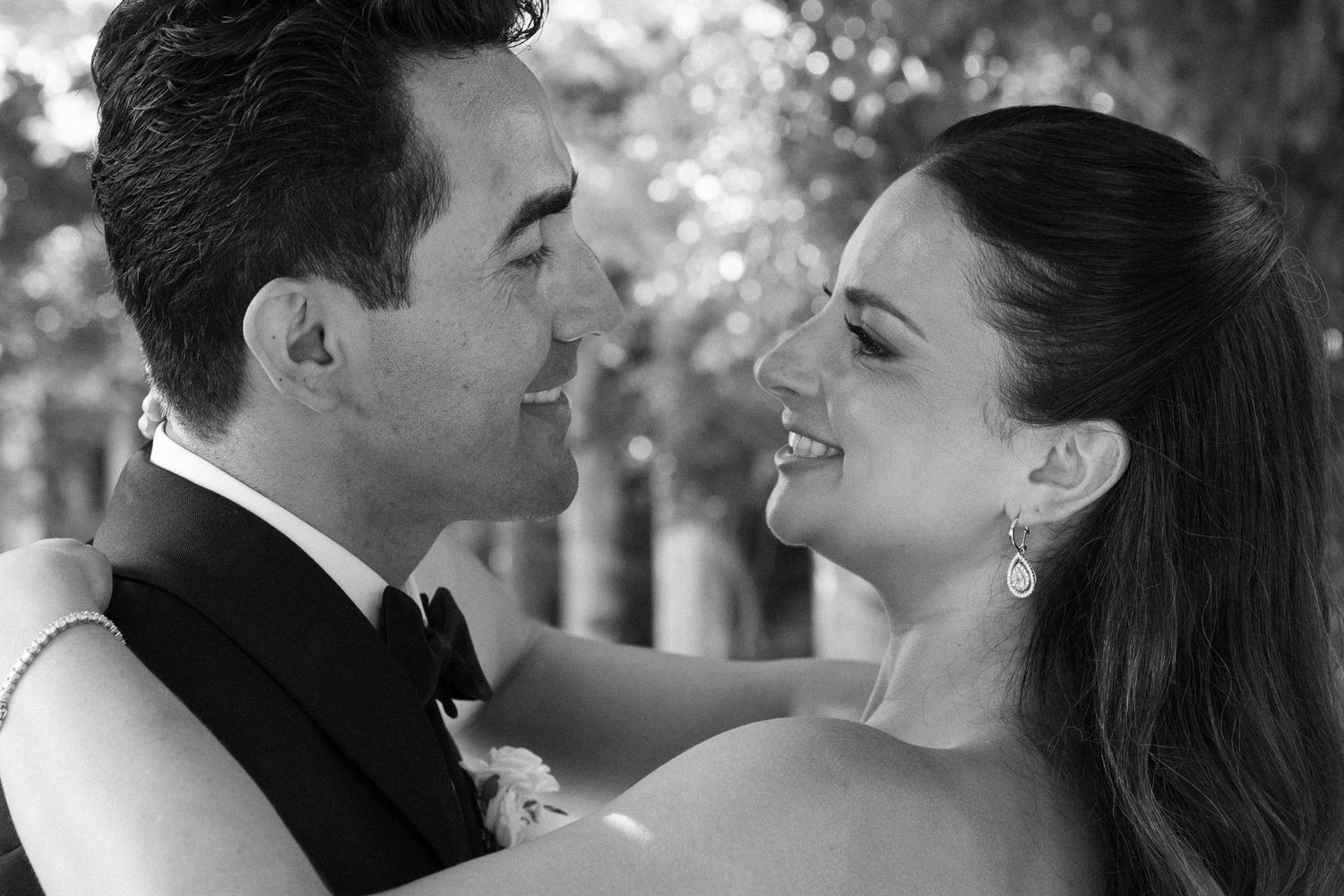 Black and white wedding photo of a smiling bride and groom gazing at each other outdoors.
