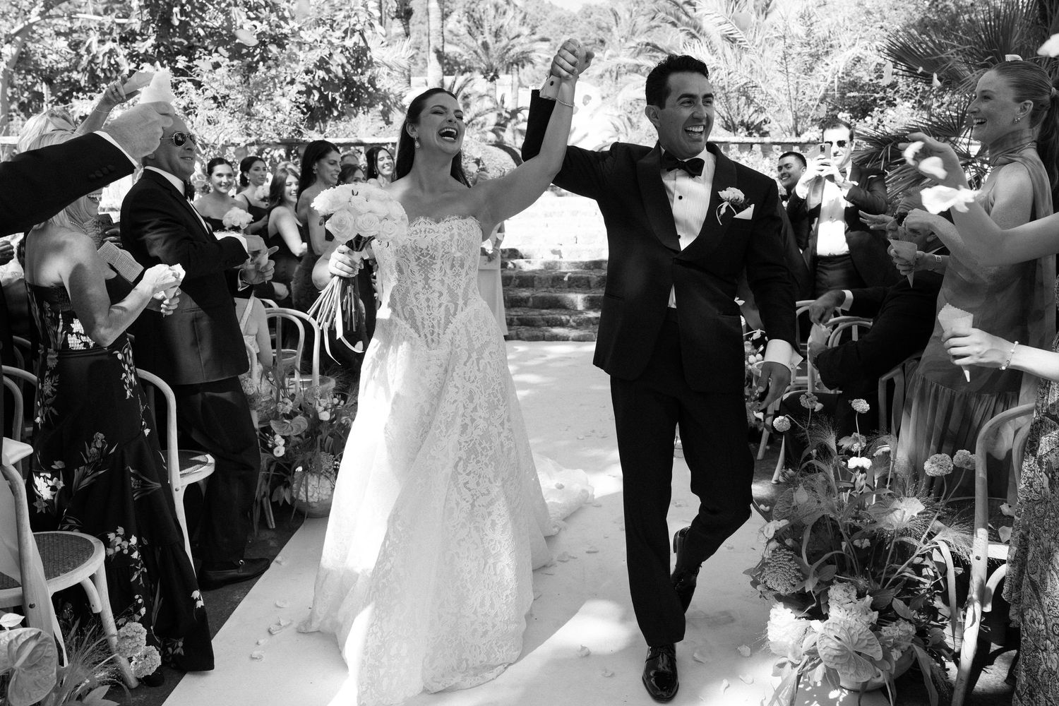 Black and white photo of a joyful bride and groom walking down the aisle after their outdoor wedding ceremony.
