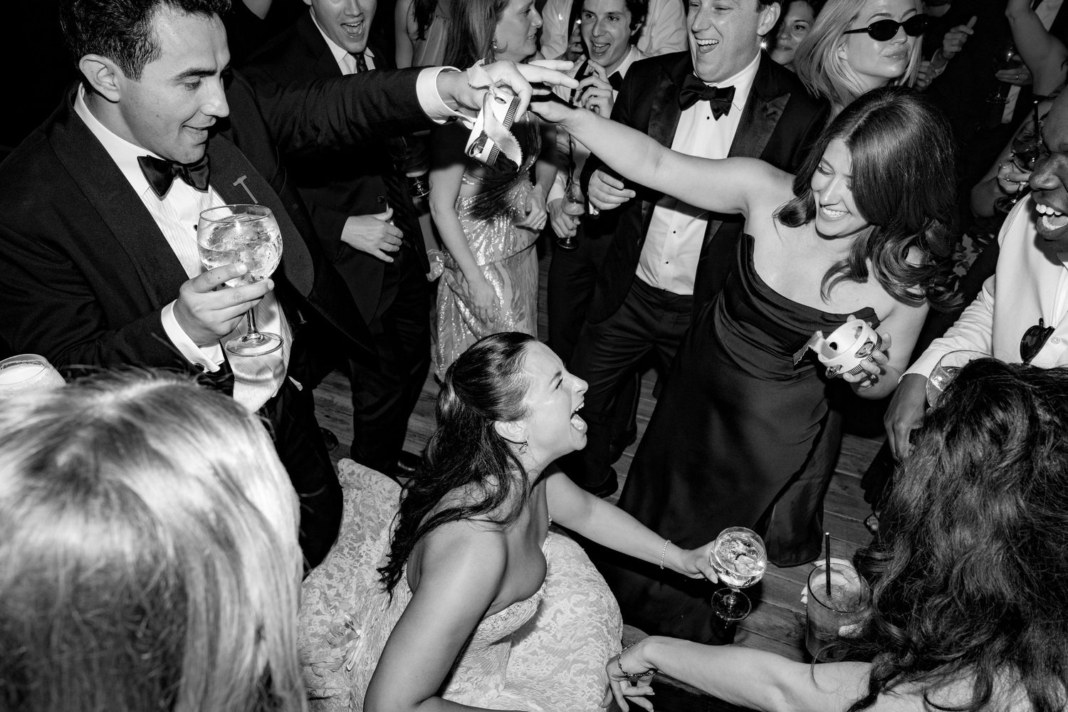 Black and white photo of wedding guests dancing and celebrating joyfully at a lively wedding reception party.