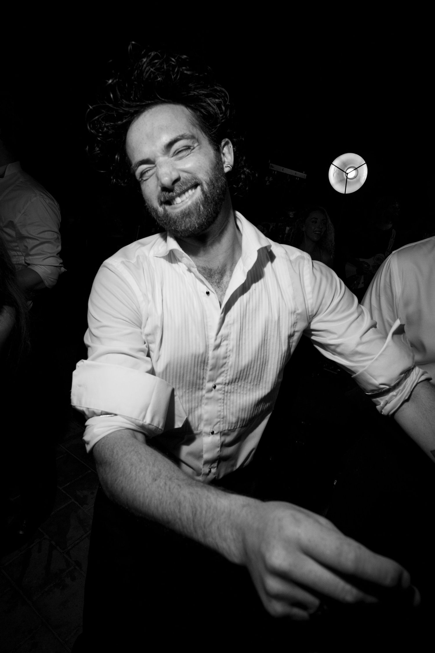 Black and white photo of a smiling bearded man in a white shirt dancing at a nightclub event.