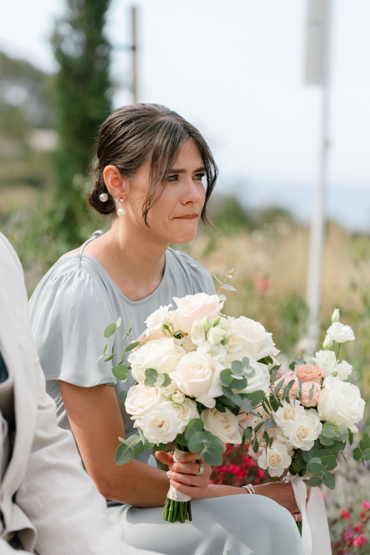 Bridesmaids in grey dresses holding elegant white rose bouquets at an outdoor ceremony.