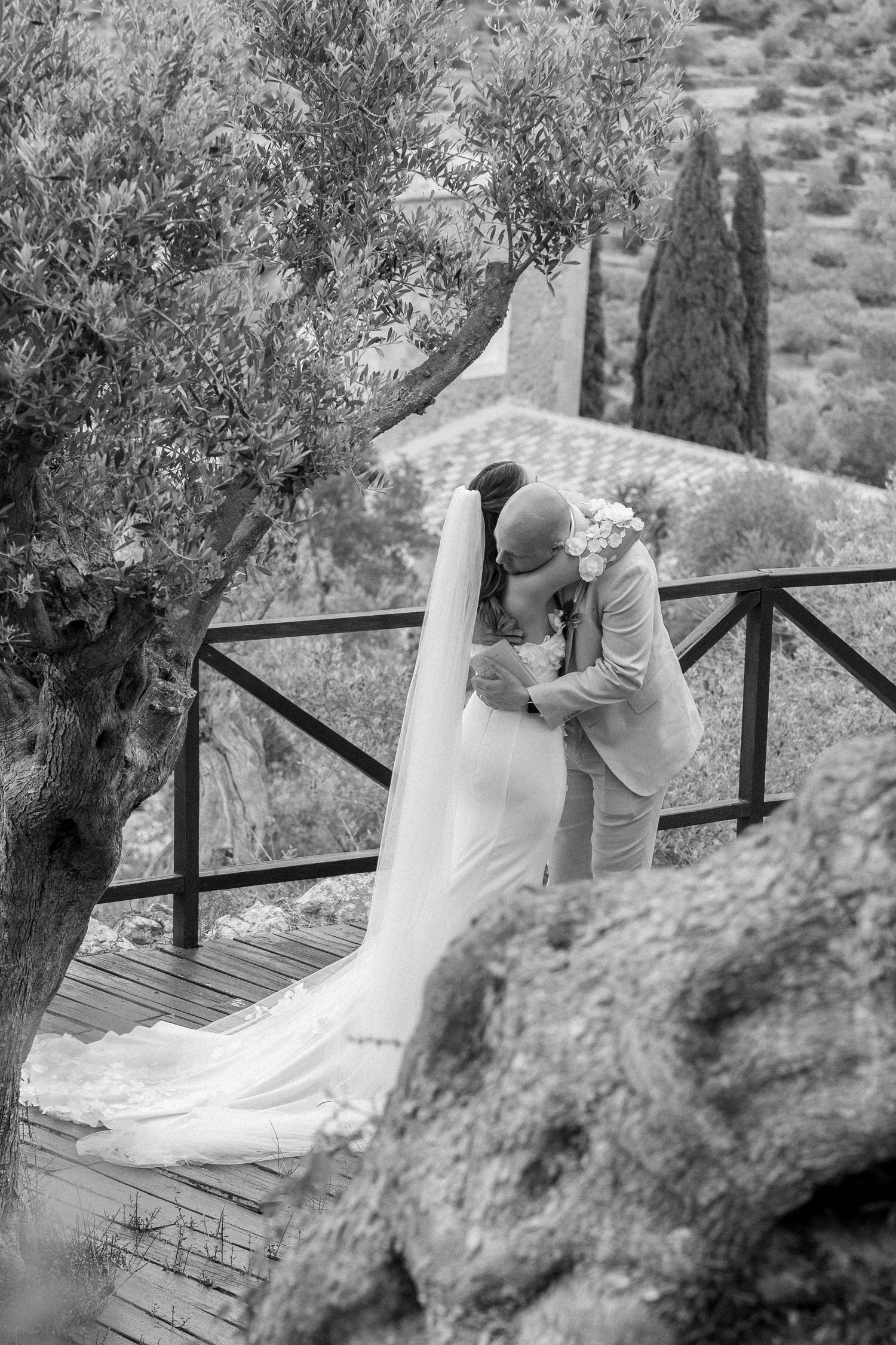 Black and white wedding photos captured on a rustic wooden deck surrounded by olive trees.