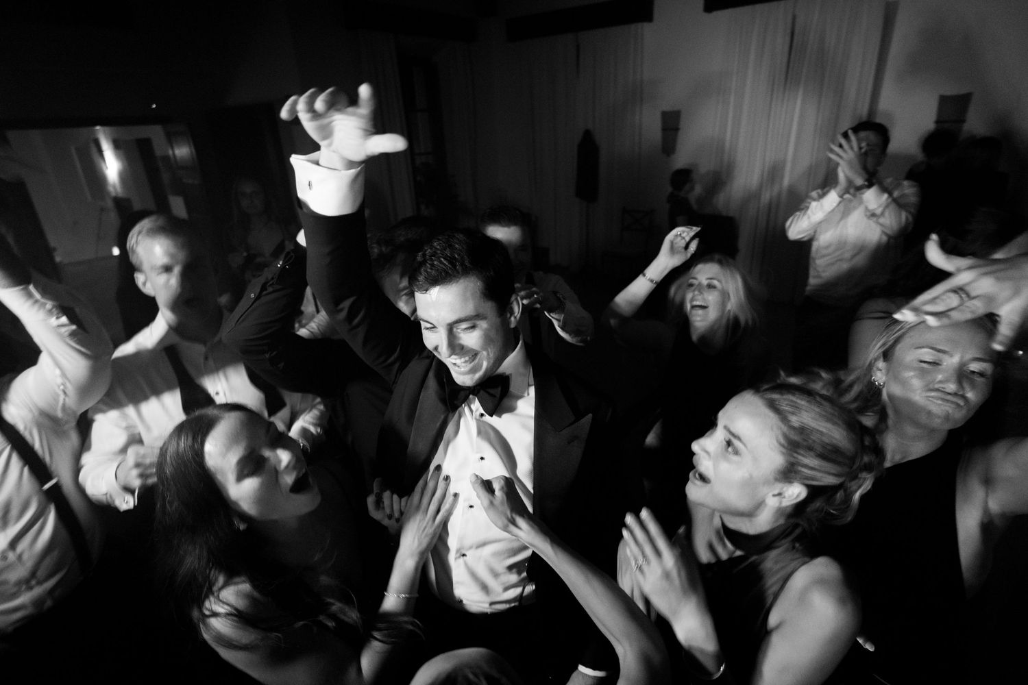 Black and white photo of a crowded dance floor with people moving energetically in a dark nightclub setting.