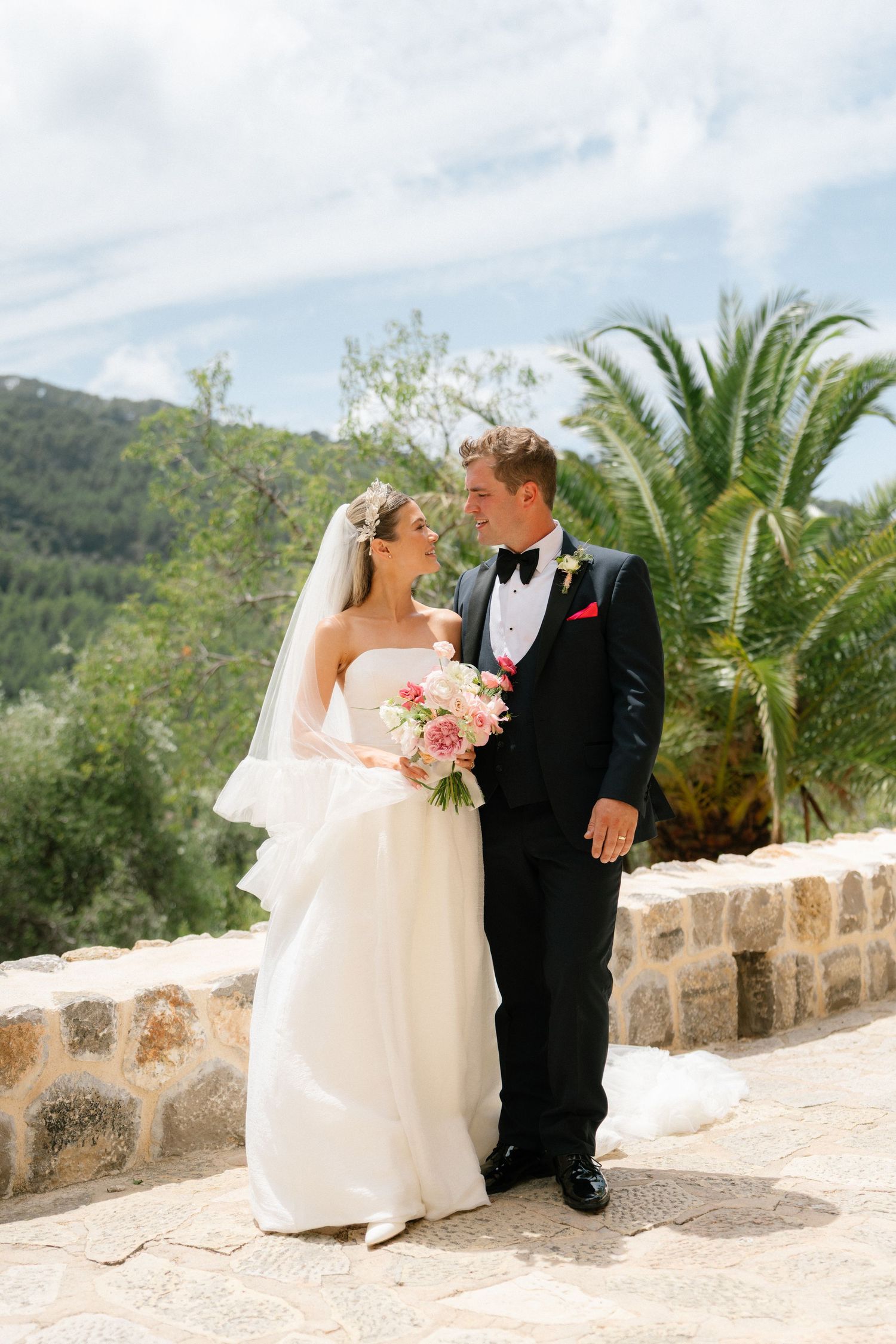 Wedding portraits on stone terrace with palm trees and mountain backdrop.