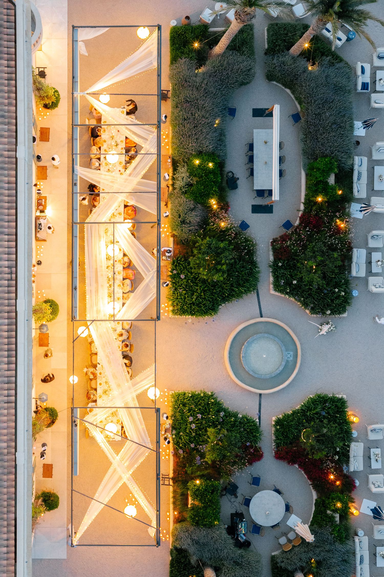 Aerial view of an illuminated courtyard with geometric patterns and landscaping at night.