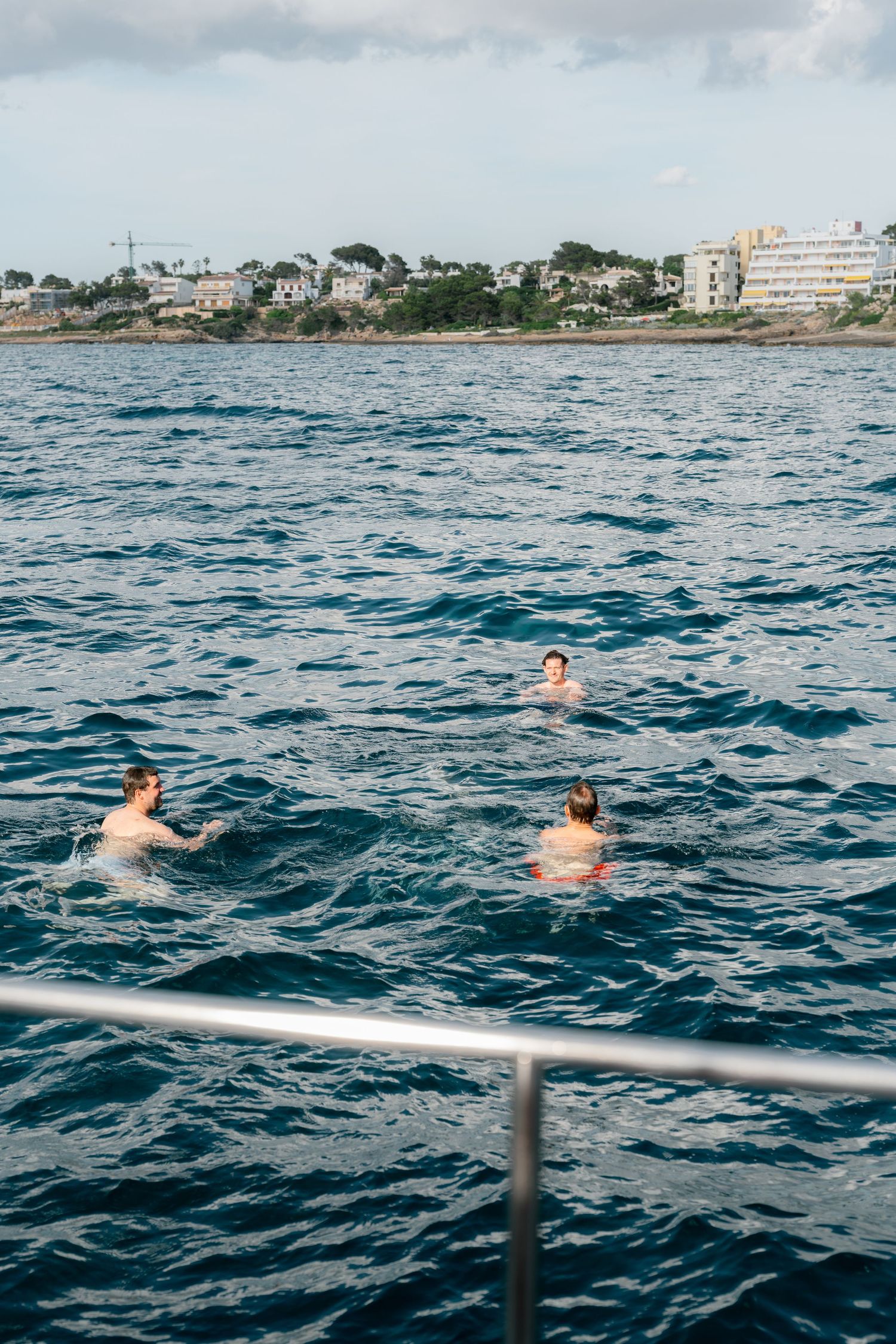 People swimming and relaxing in blue ocean waters near a coastal town.