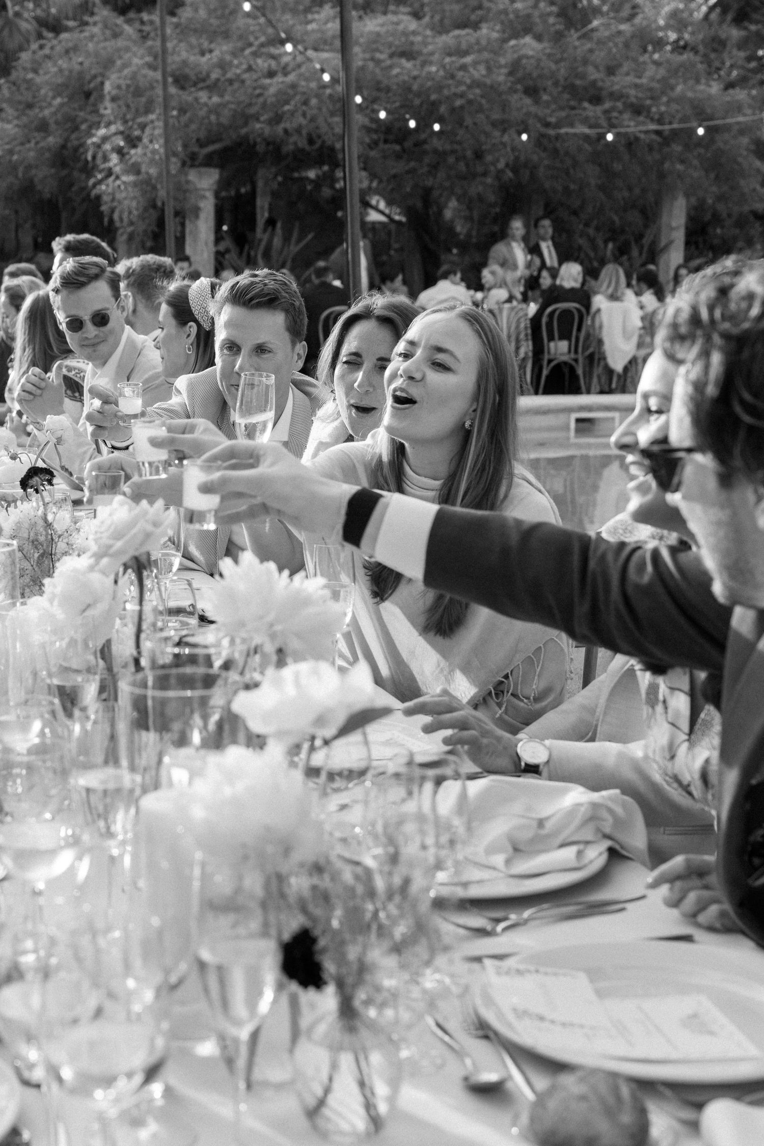 Wedding guests raise wine glasses for a toast across a beautifully decorated outdoor dining table.