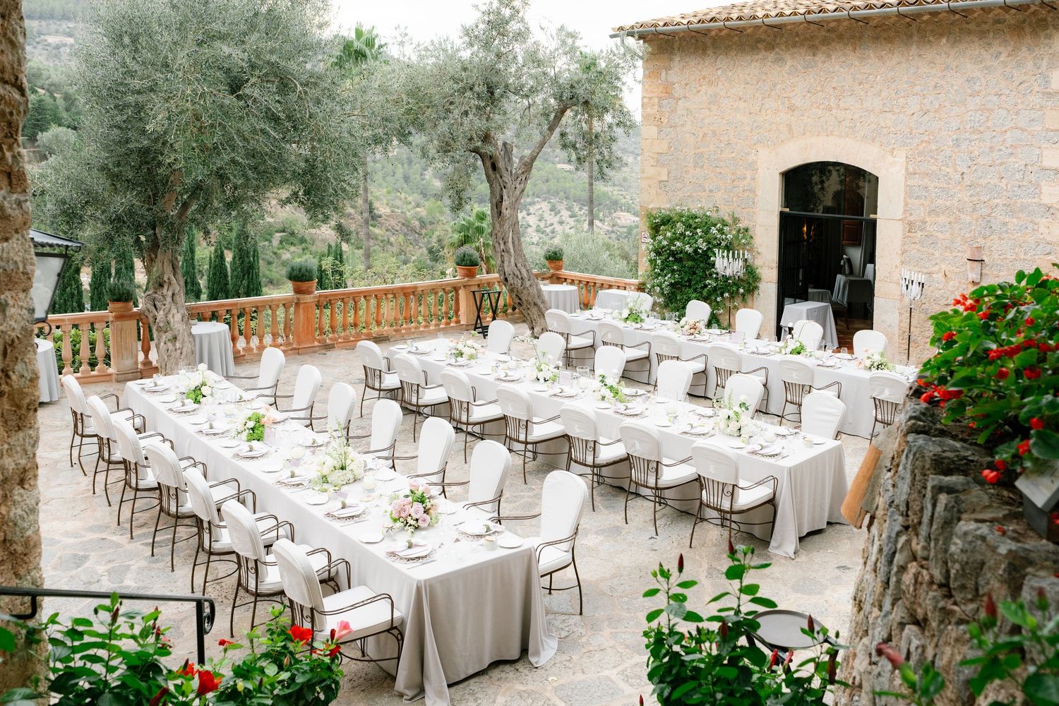 Wedding reception venue with rustic stone walls and elegant table settings under olive trees.