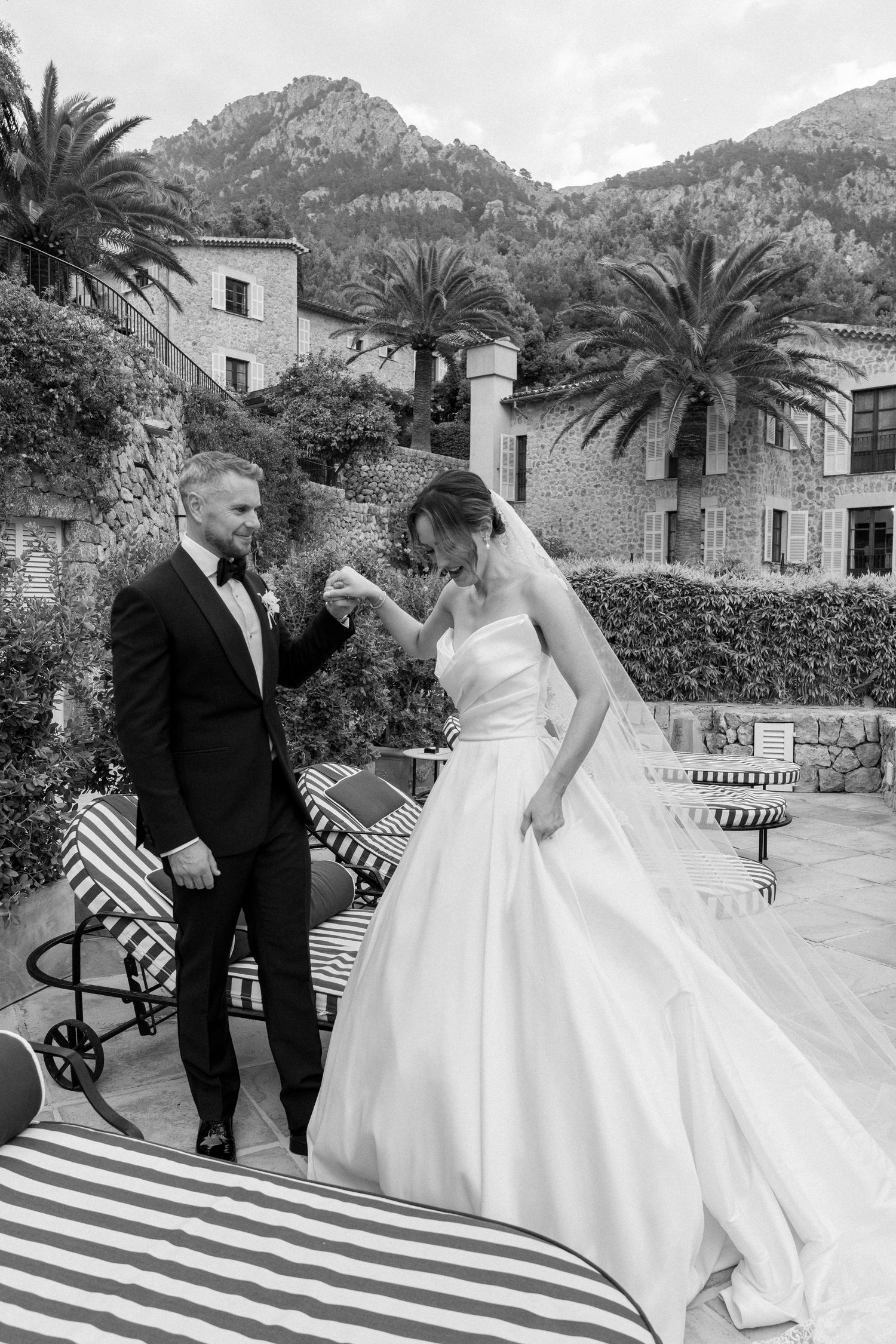 A wedding couple shares a romantic moment on a terrace with mountain views and palm trees in the background.