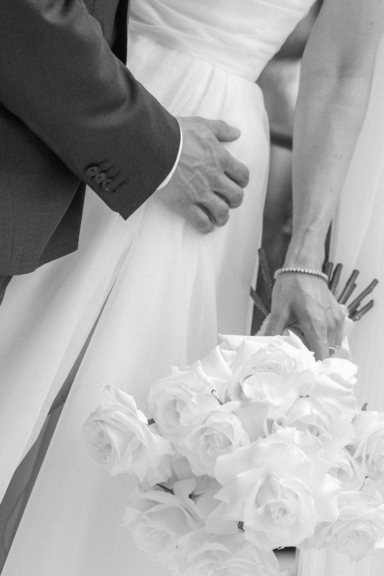 Close-up black and white details of bride holding white rose wedding bouquet.