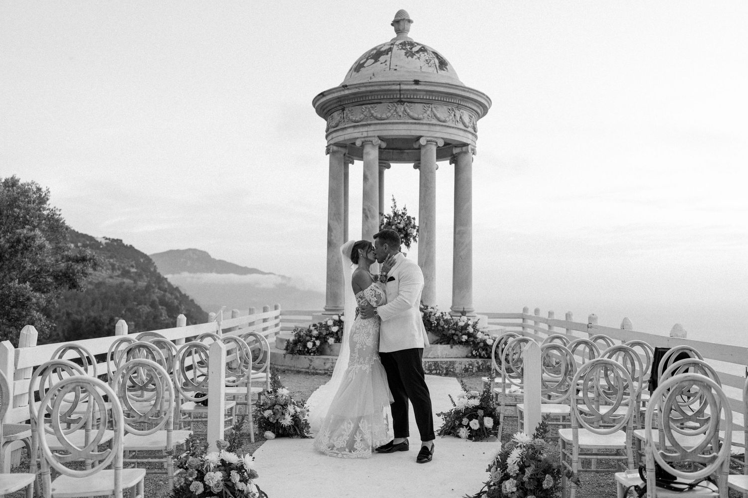 Elegant wedding ceremony setup with white columns and ocean views on a scenic terrace.