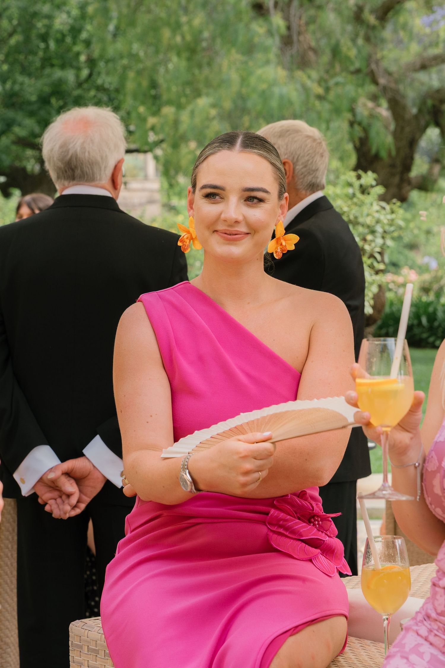 Wedding guest in bright pink dress enjoying drinks at an outdoor reception.