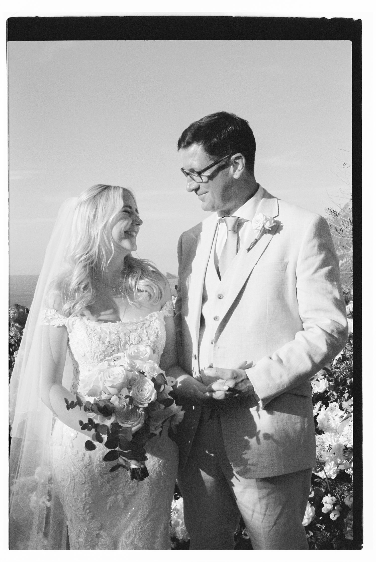 Black and white portrait of newlyweds holding bouquet against scenic mountain backdrop.