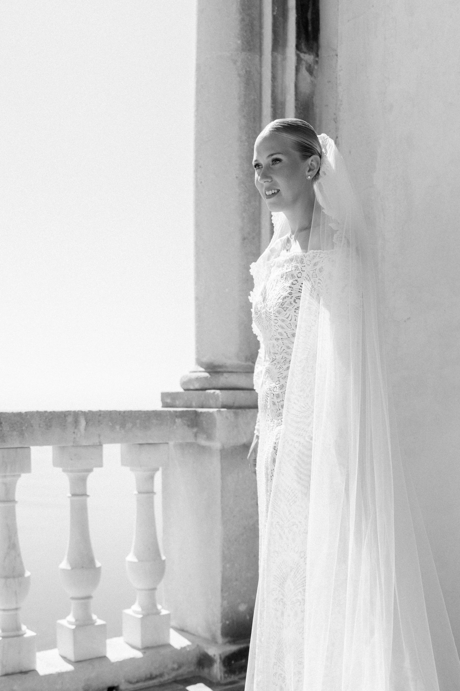 Classic bridal portrait in white lace gown against a colonnade with dramatic lighting.