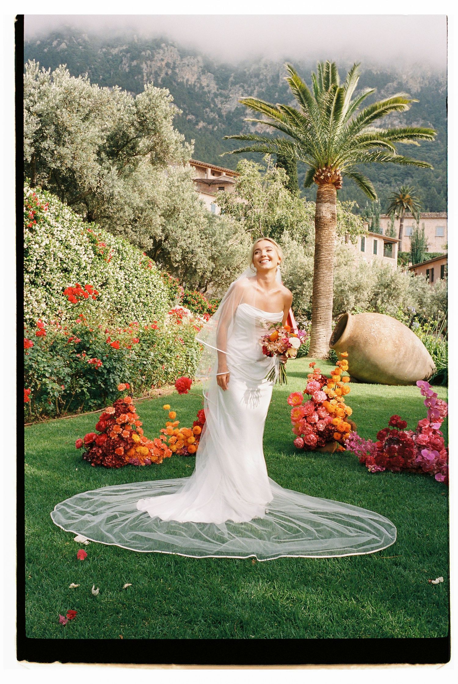 Wedding portrait in a Mediterranean garden with colorful flowers and a tall palm tree.
