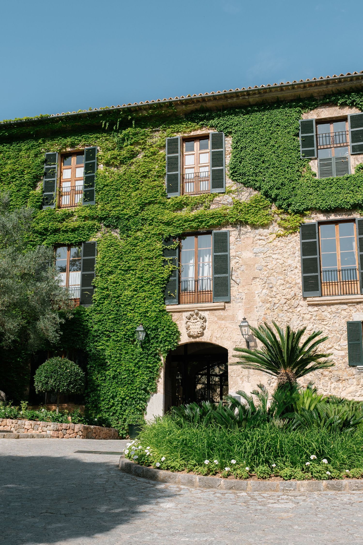 Grand Hotel Son Net covered in lush green ivy with wooden shuttered windows and tropical plants in Mallorca, Spain.