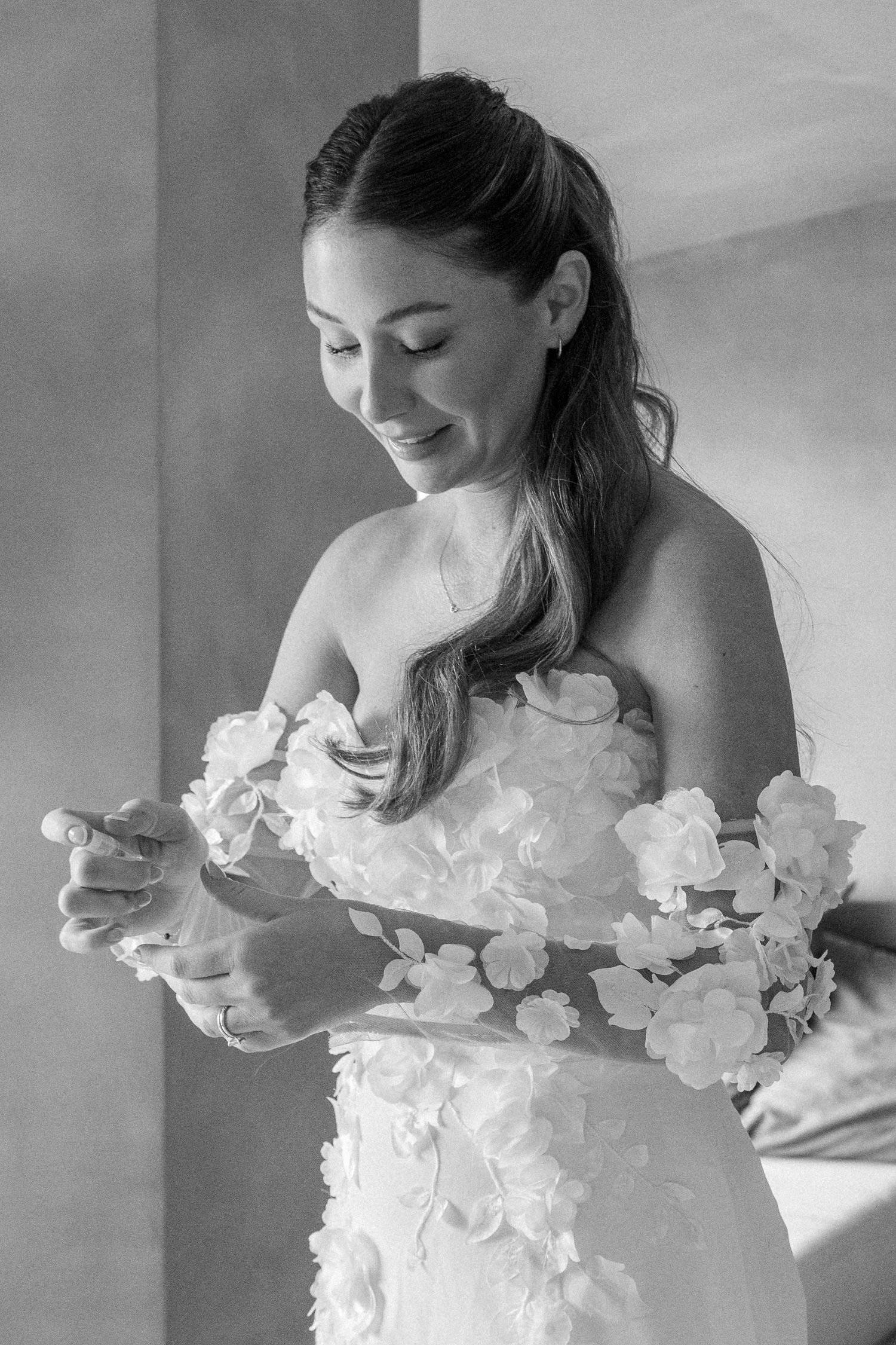 Black and white portrait of bride admiring floral details on her wedding gown.