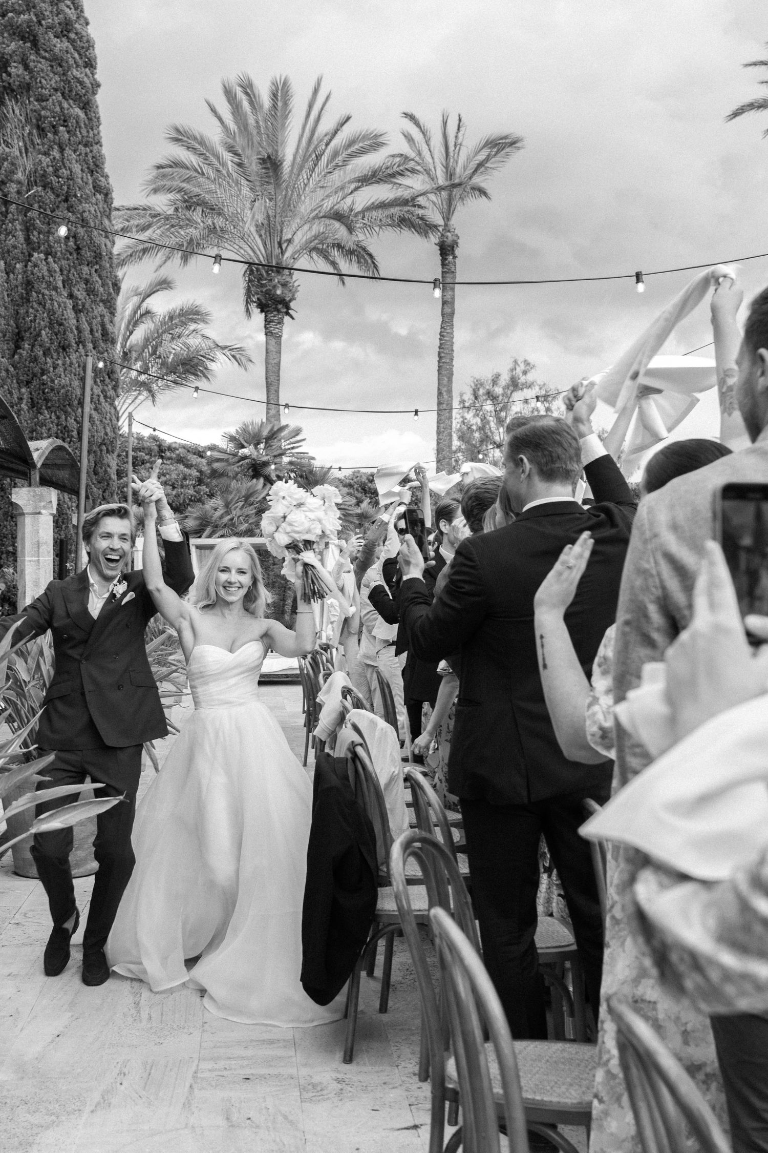 Wedding celebration with guests dancing under palm trees and string lights.