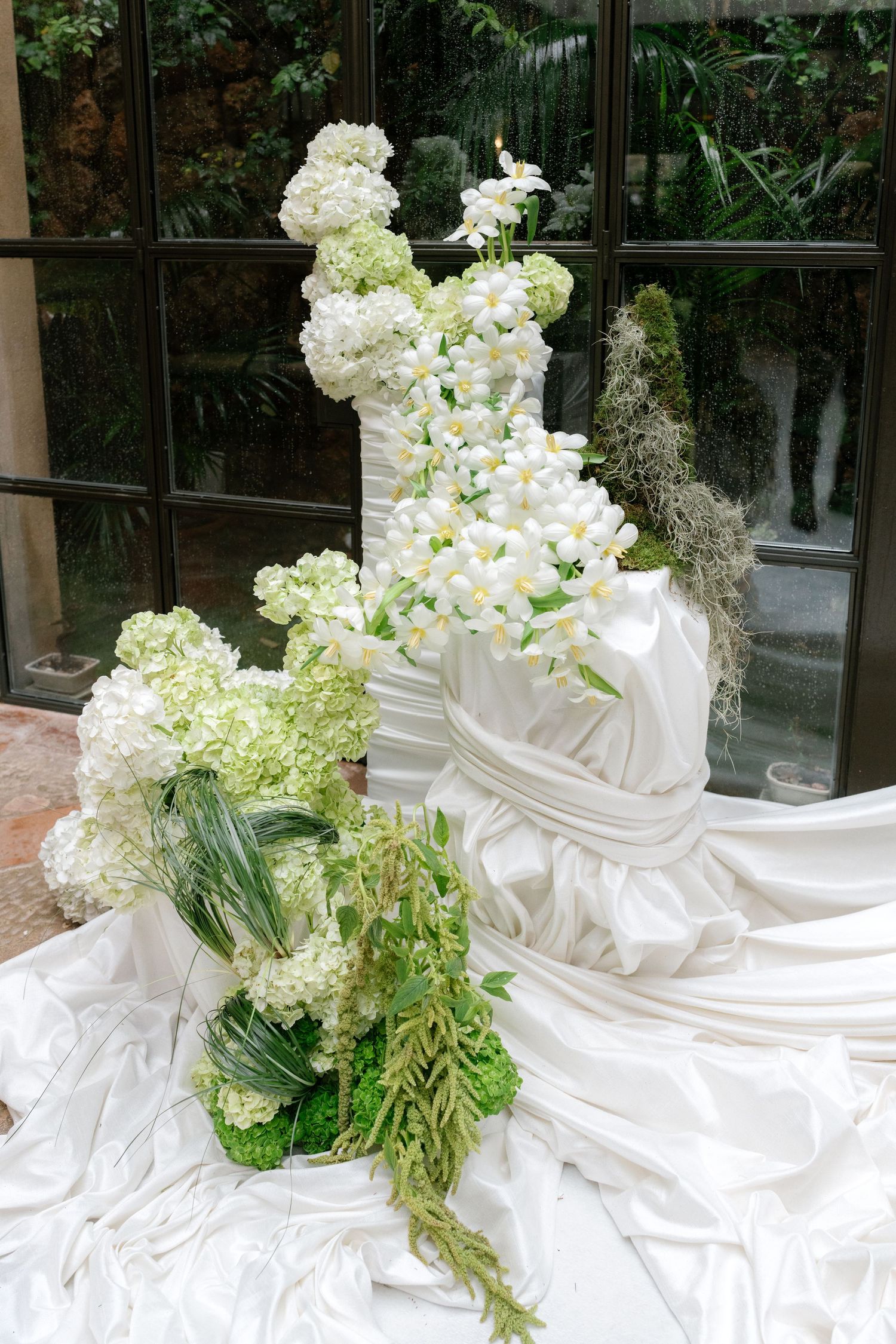 Elegant white floral arrangements with hydrangeas and greenery line a glass window display.