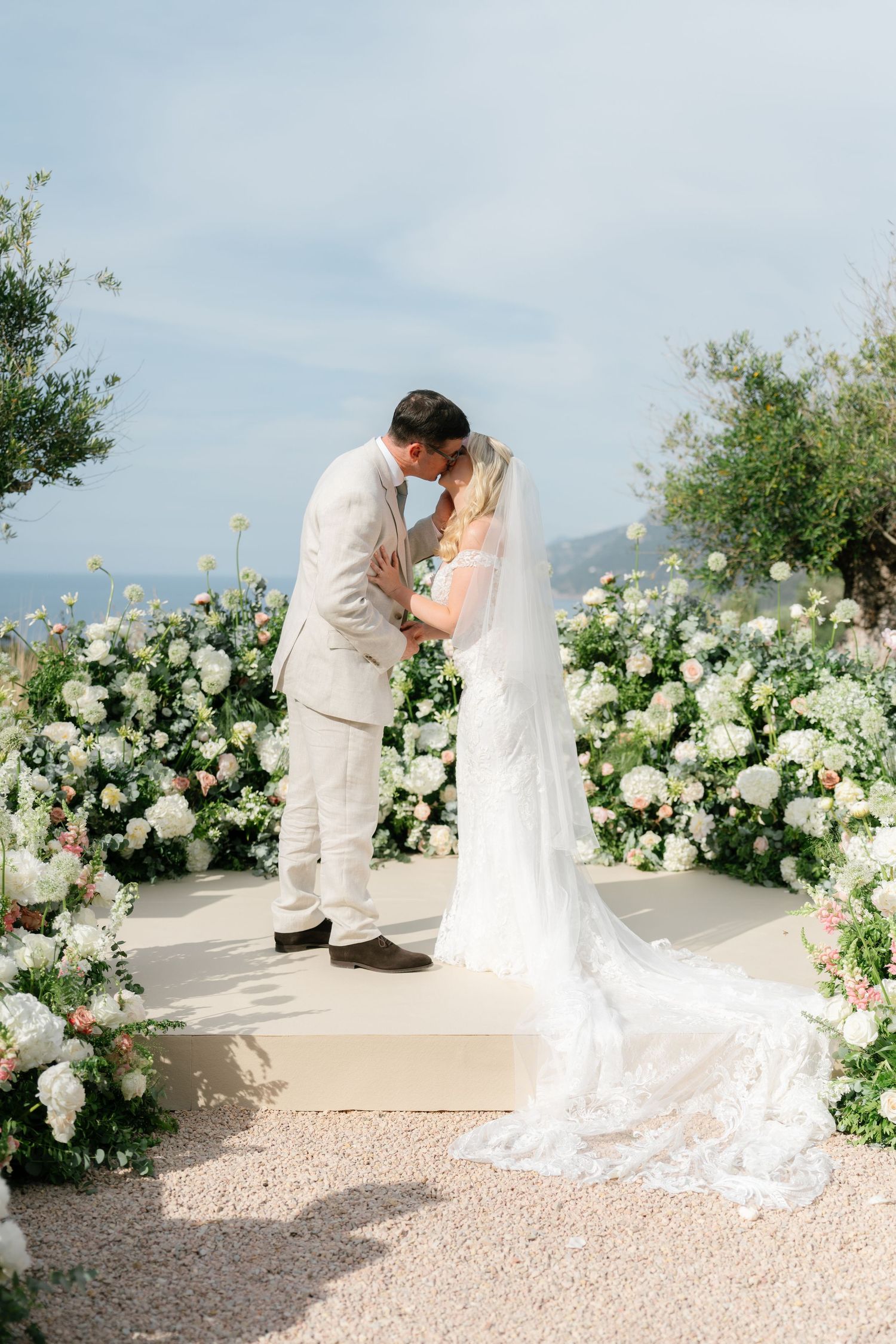 Romantic wedding ceremony moment with white floral arch and mountain backdrop.