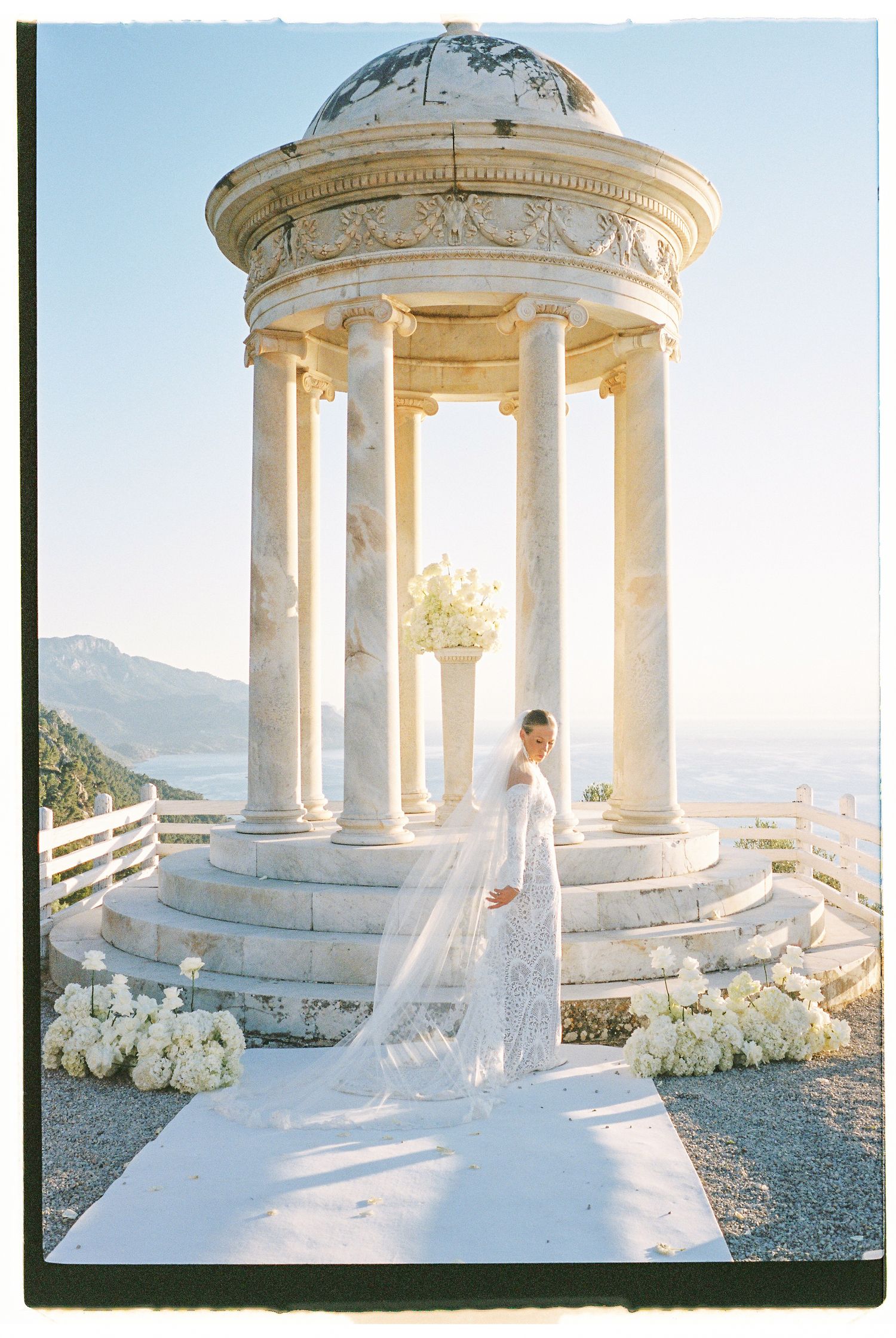 Elegant white marble gazebo with columns overlooking coastal views during a romantic wedding ceremony.