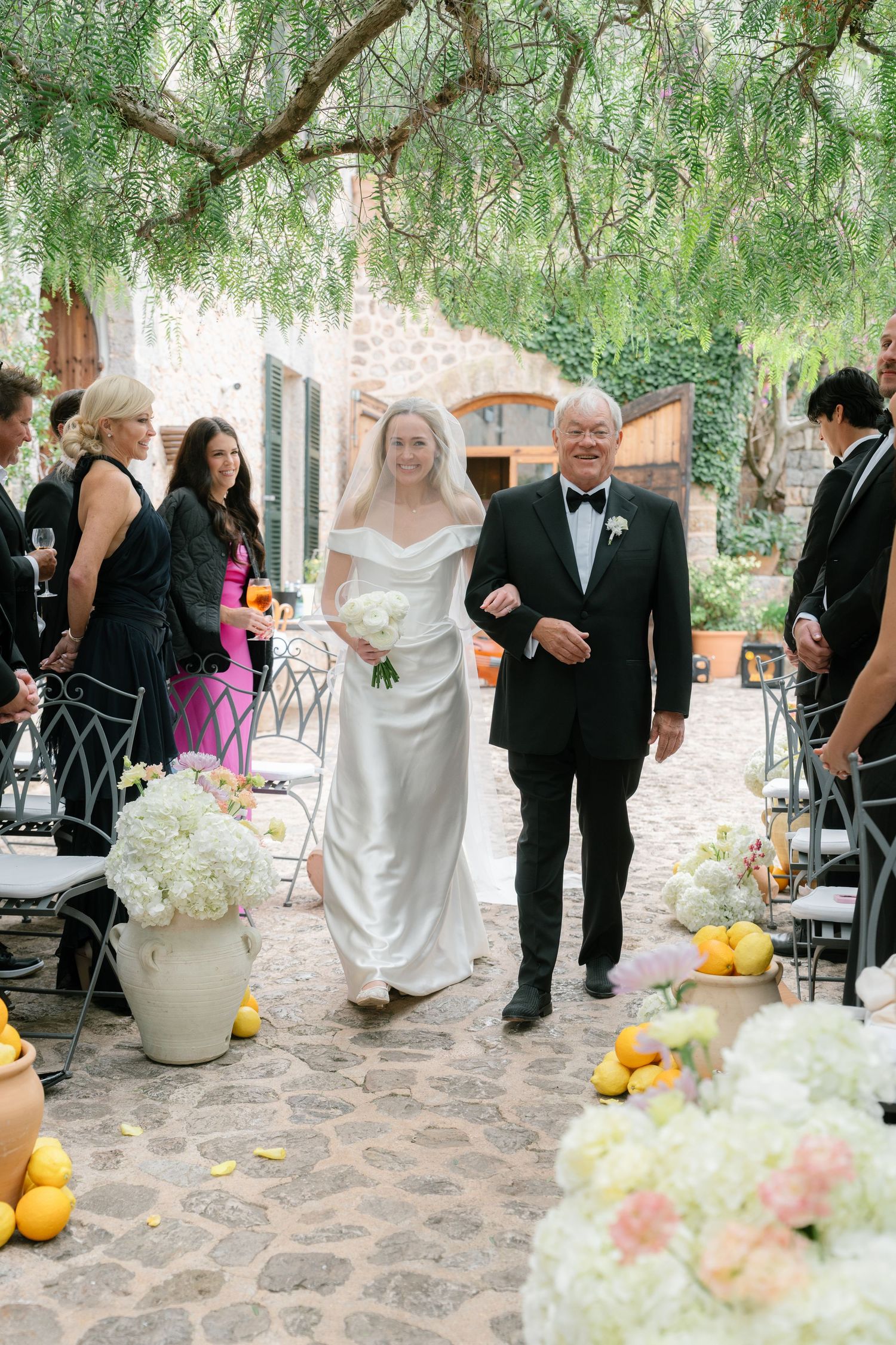 Elegant outdoor wedding reception setup with white floral arrangements and citrus decor on stone patio.