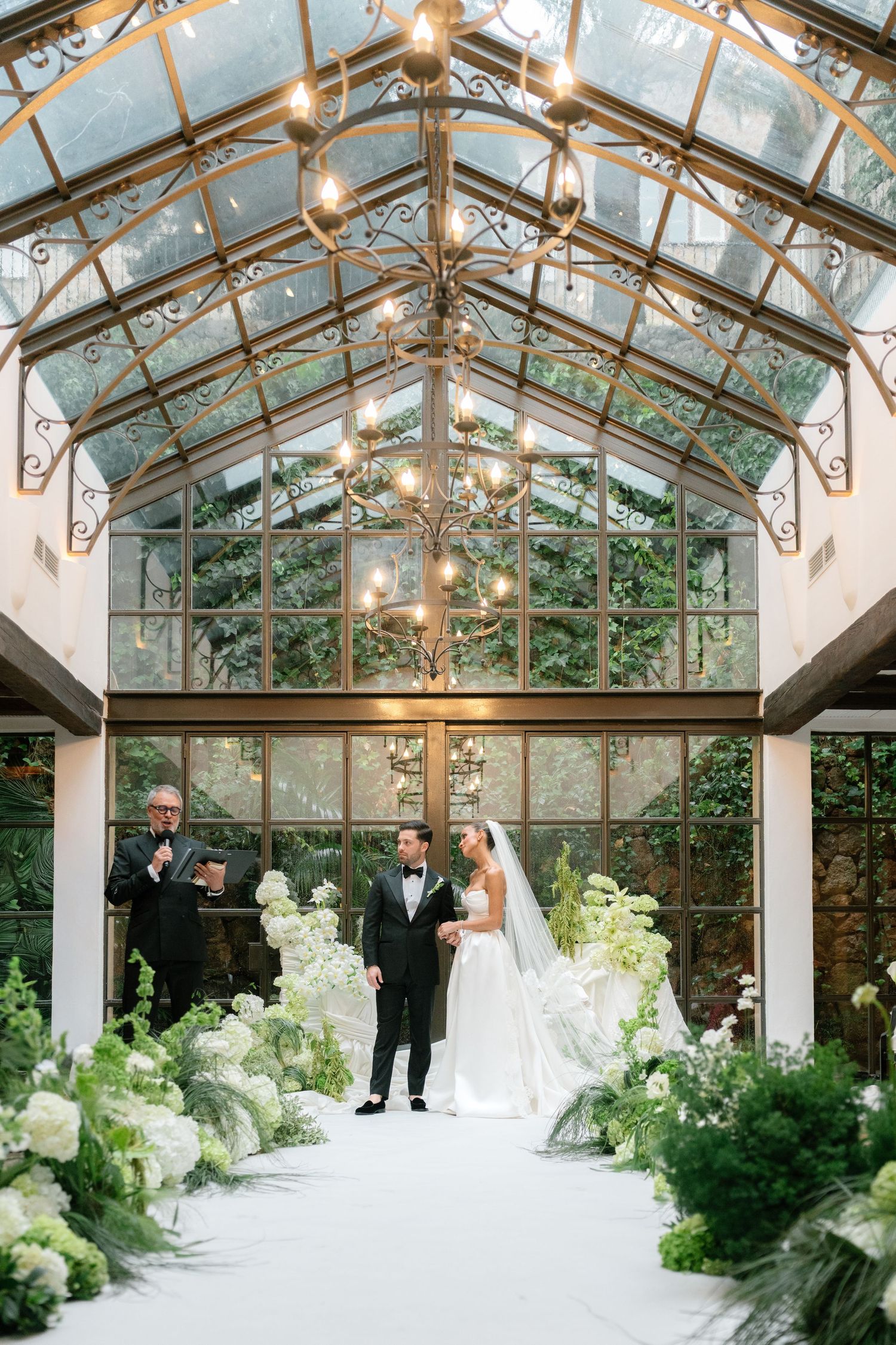 Greenhouse wedding ceremony space with white floral arrangements and hanging lights creating romantic ambiance.