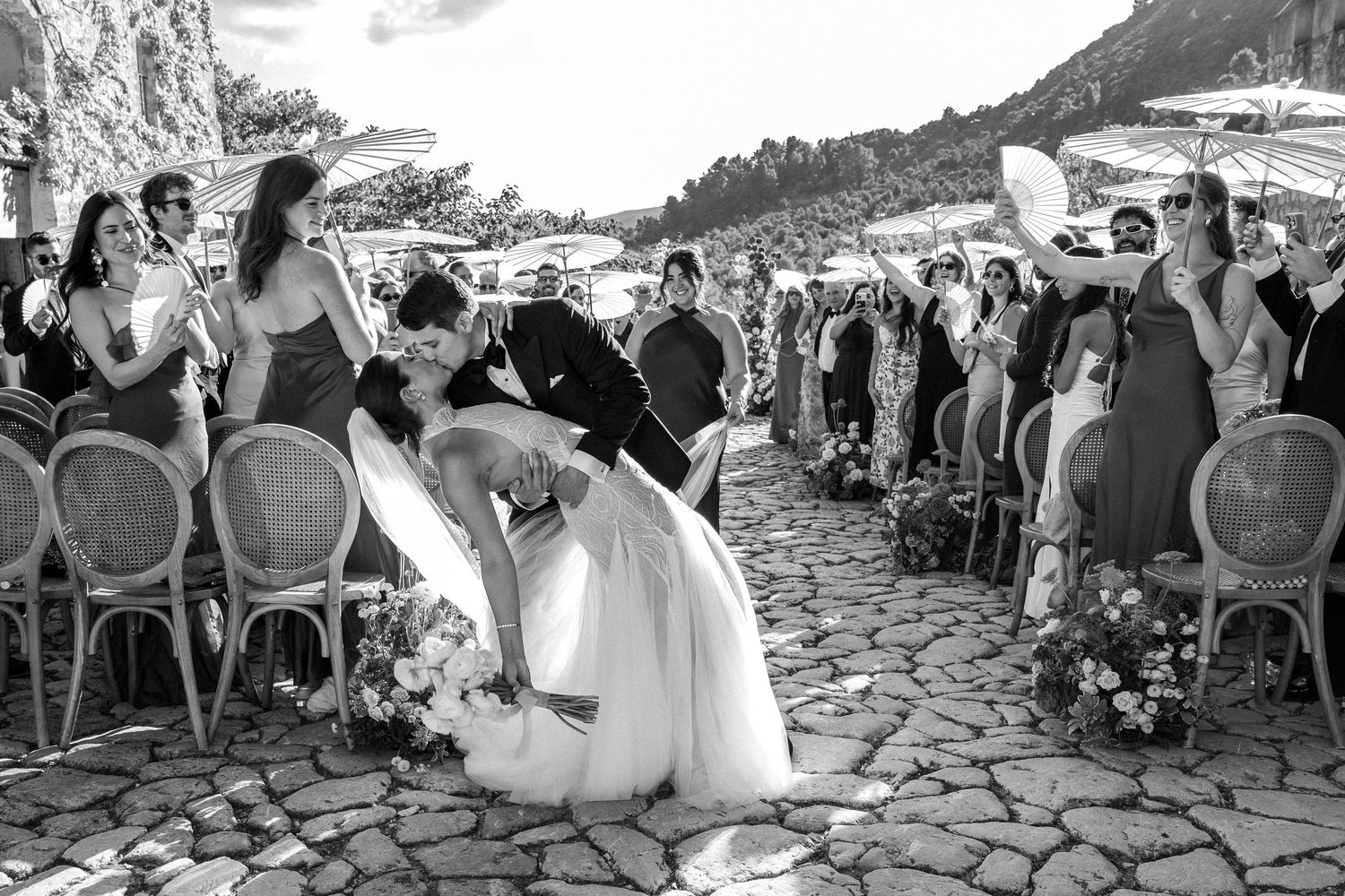 Panoramic view of wedding ceremony guests seated on stone terrace with mountain backdrop.