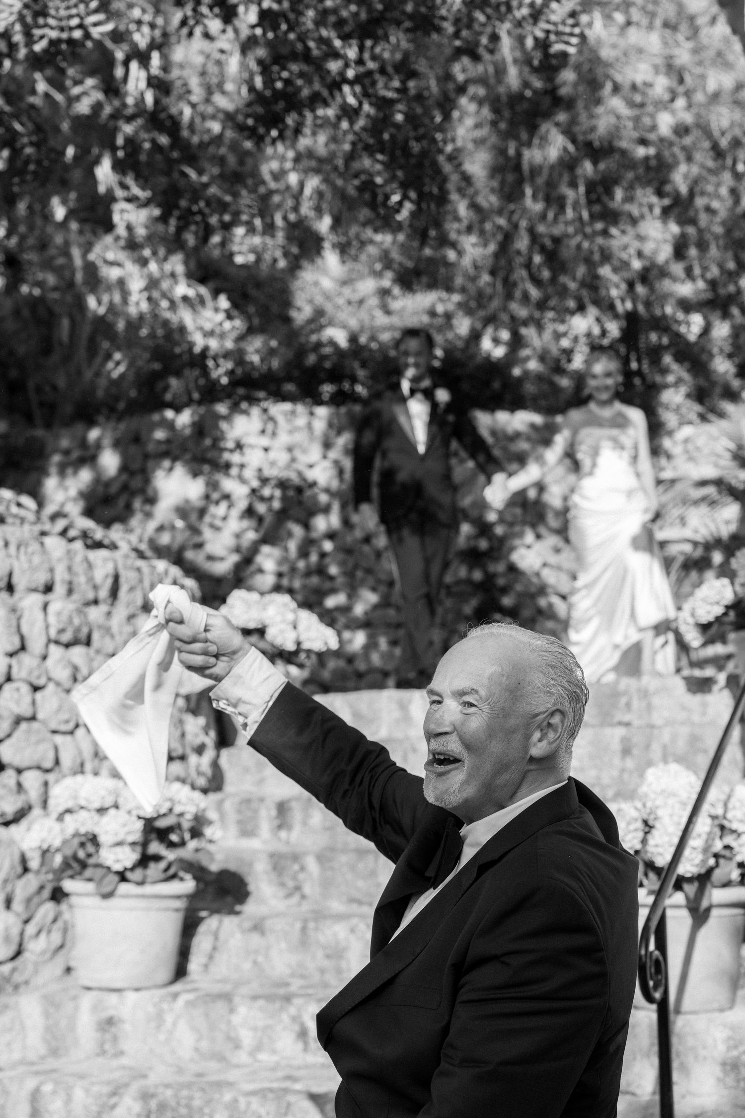 Wedding guests in formal attire celebrating joyfully in a garden setting.