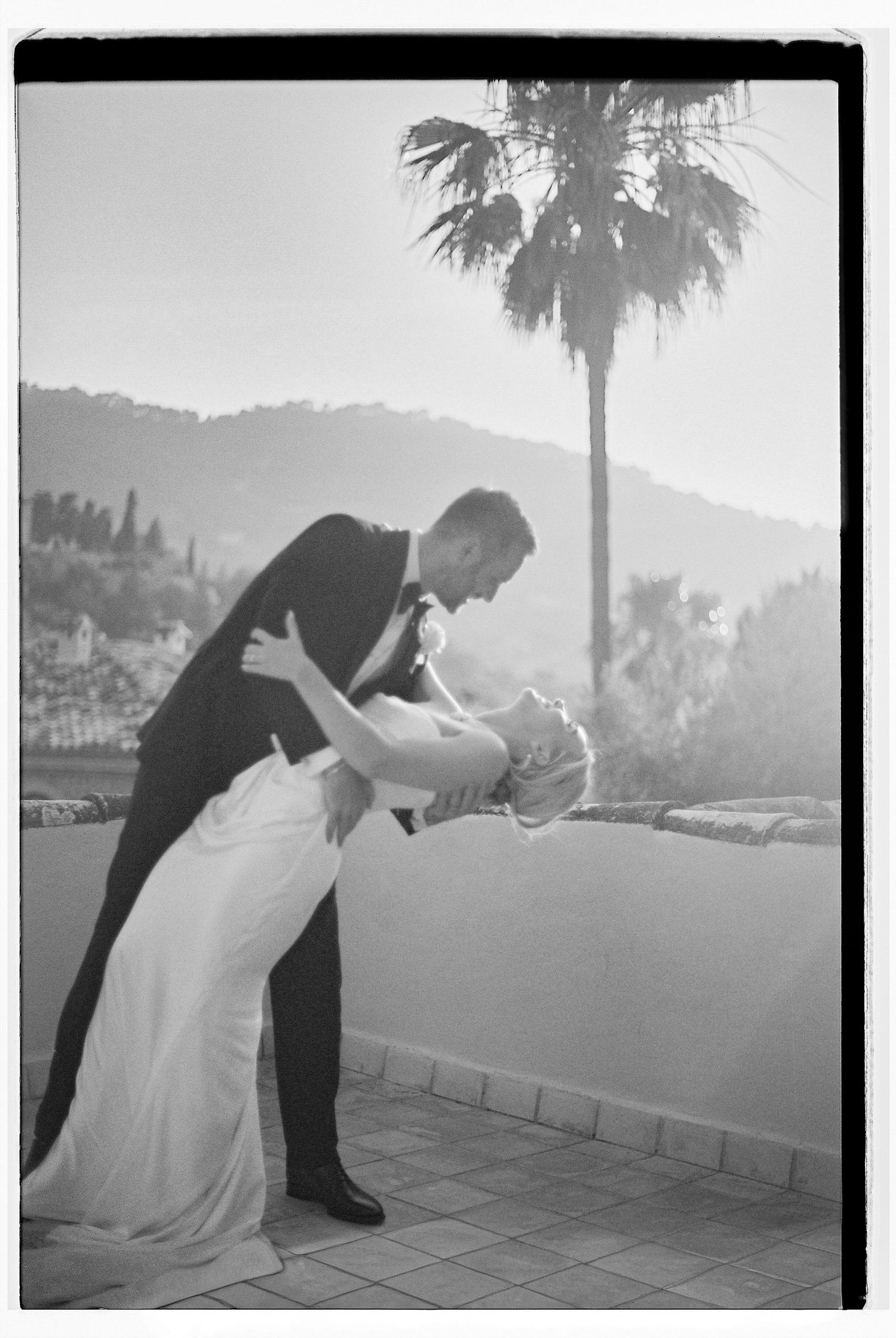 A couple in formal wedding attire dips dramatically against a scenic mountain background.