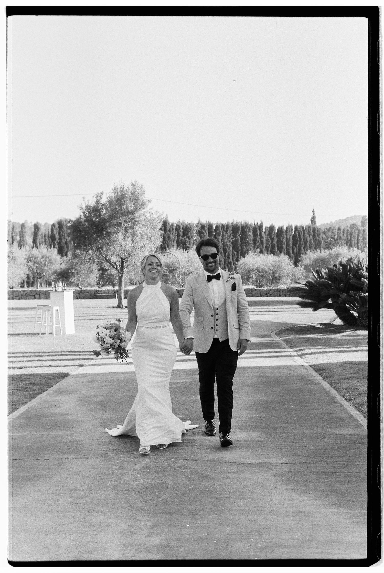 A couple walking together on a garden path in formal attire.