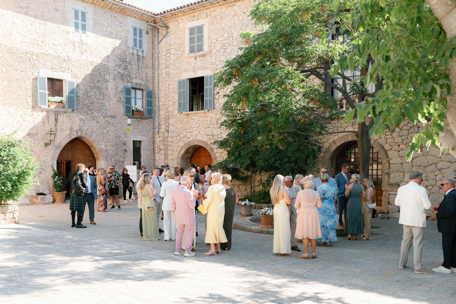 Wedding guests gathering in a Mediterranean courtyard with stone architecture.