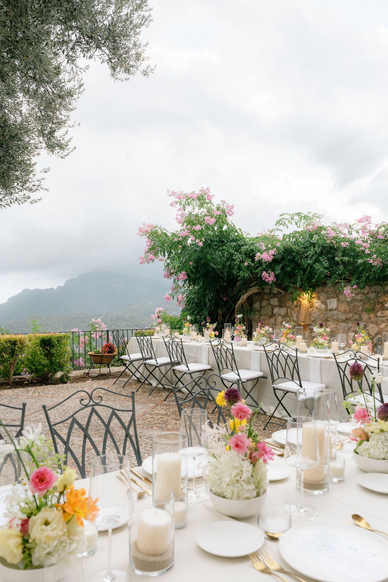 Elegant outdoor wedding reception tables set with delicate floral centerpieces and white linens against a mountain backdrop.